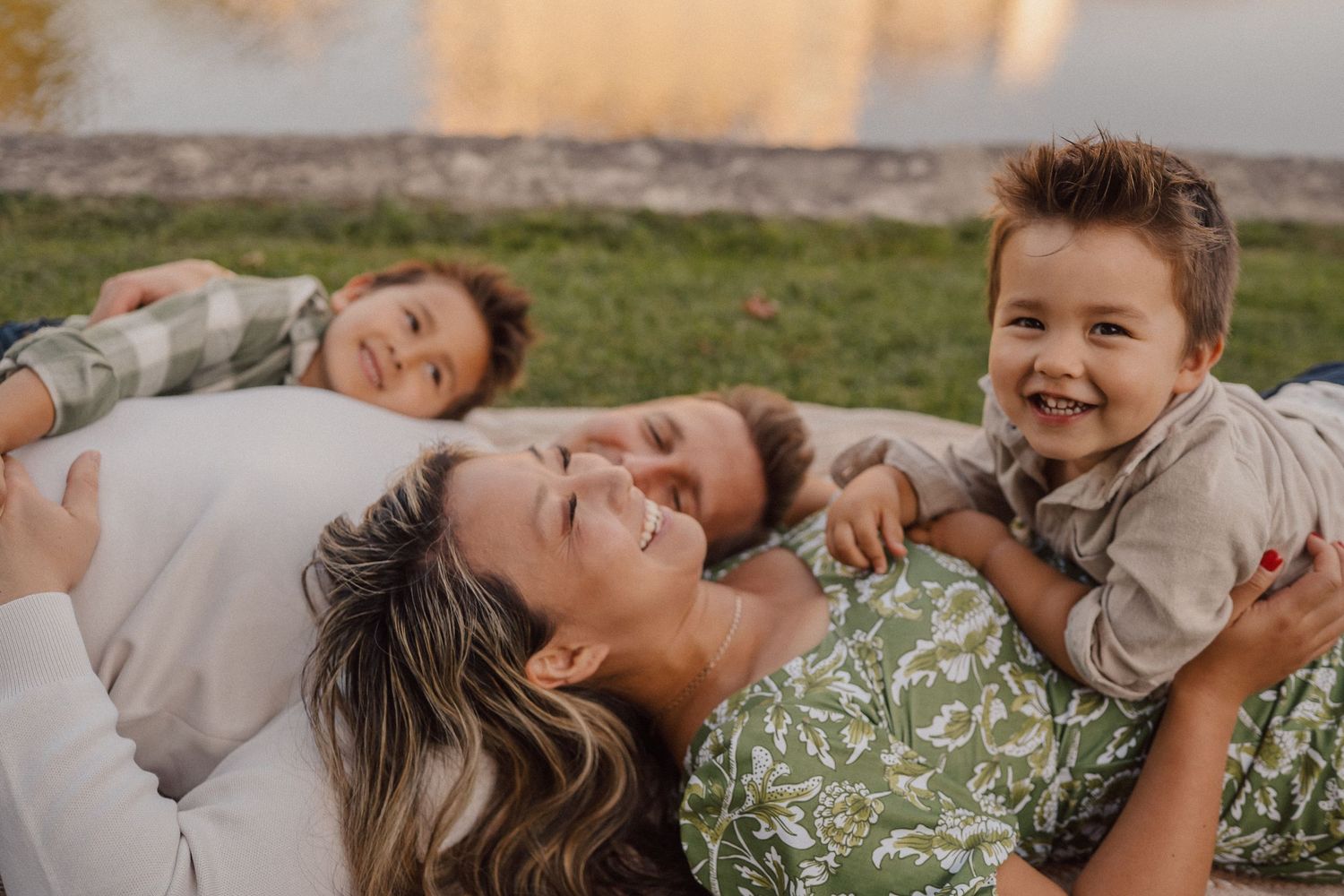 Family members lie together on grass during golden hour sunset photography session.