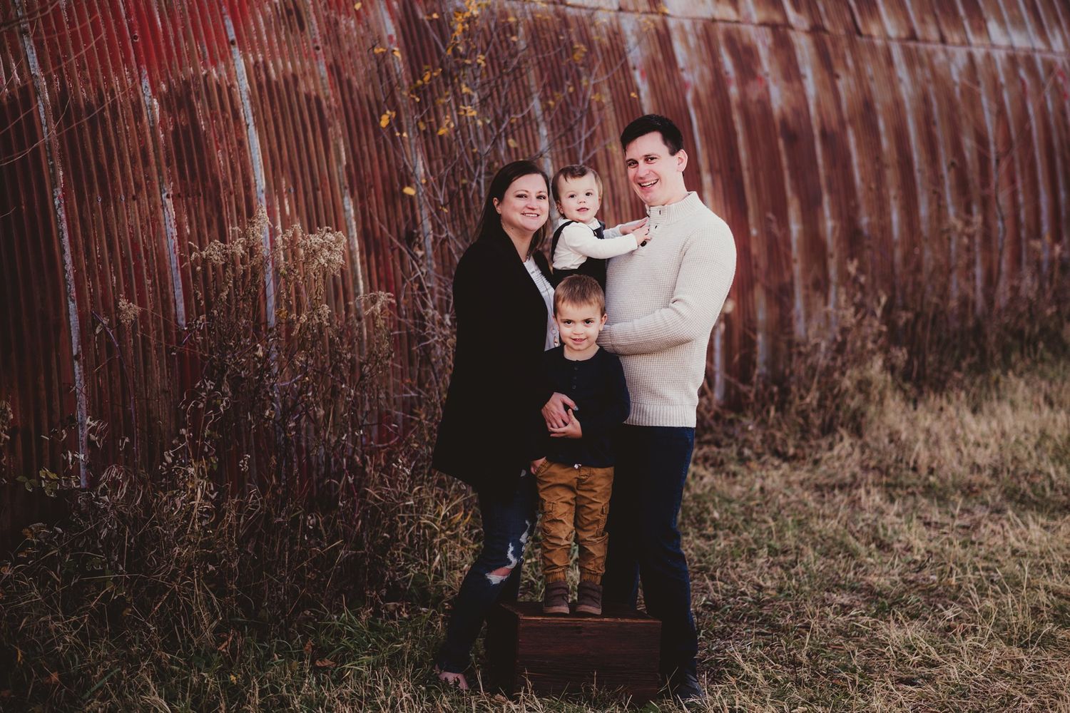 Family portrait with vintage wooden crate against weathered red barn.
