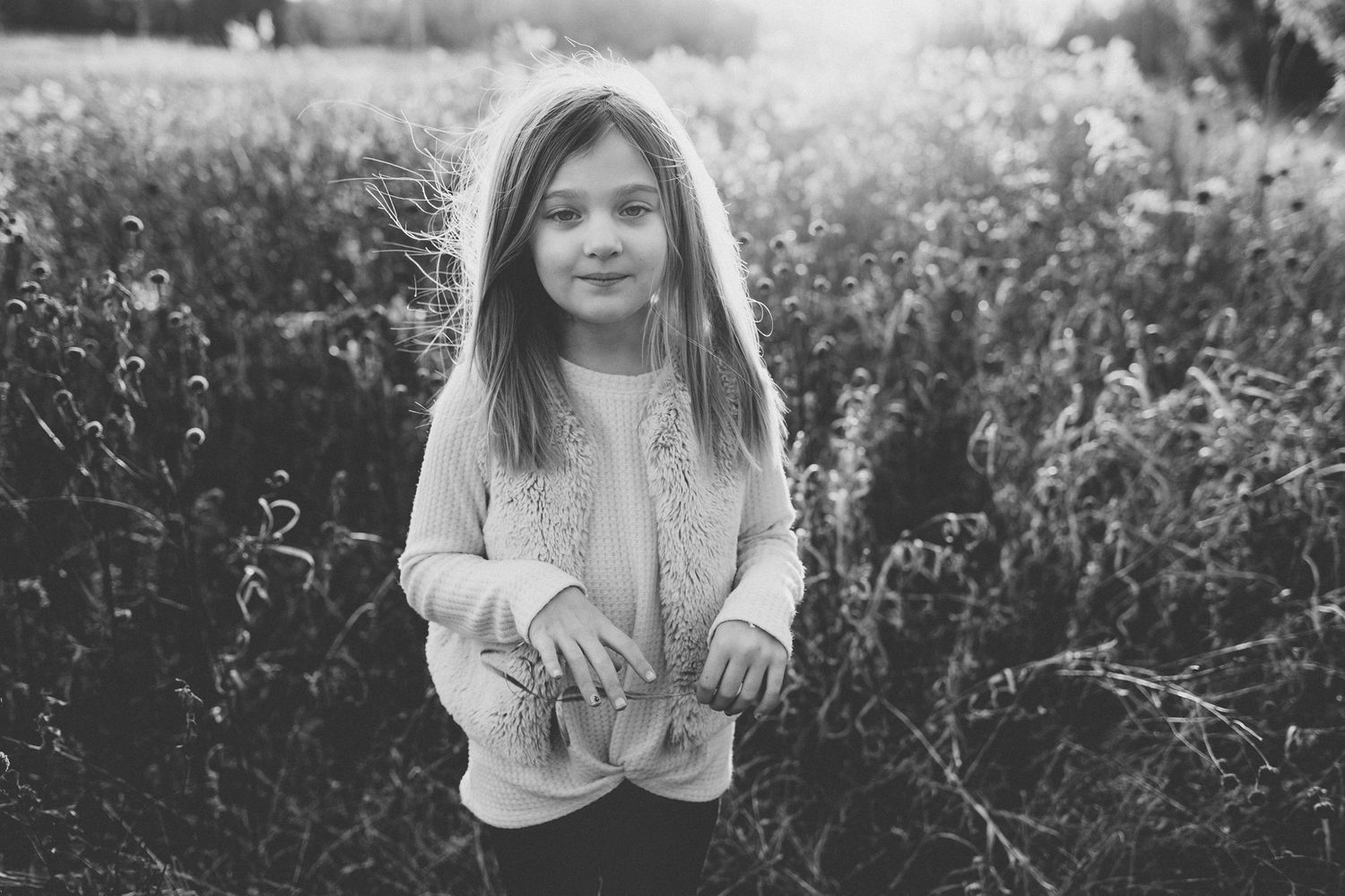 Black and white portrait of a child standing in a field of wildflowers at sunset.