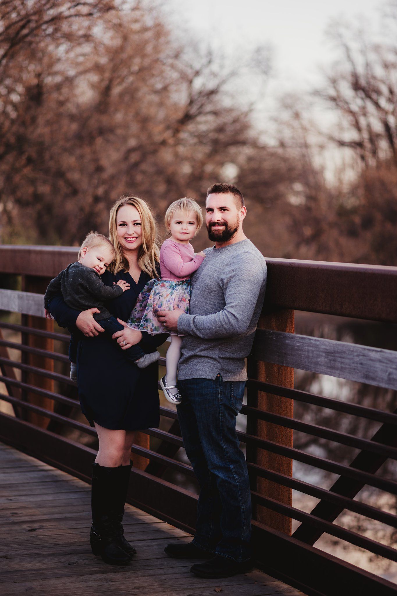 Family of four poses together on wooden bridge during fall season.