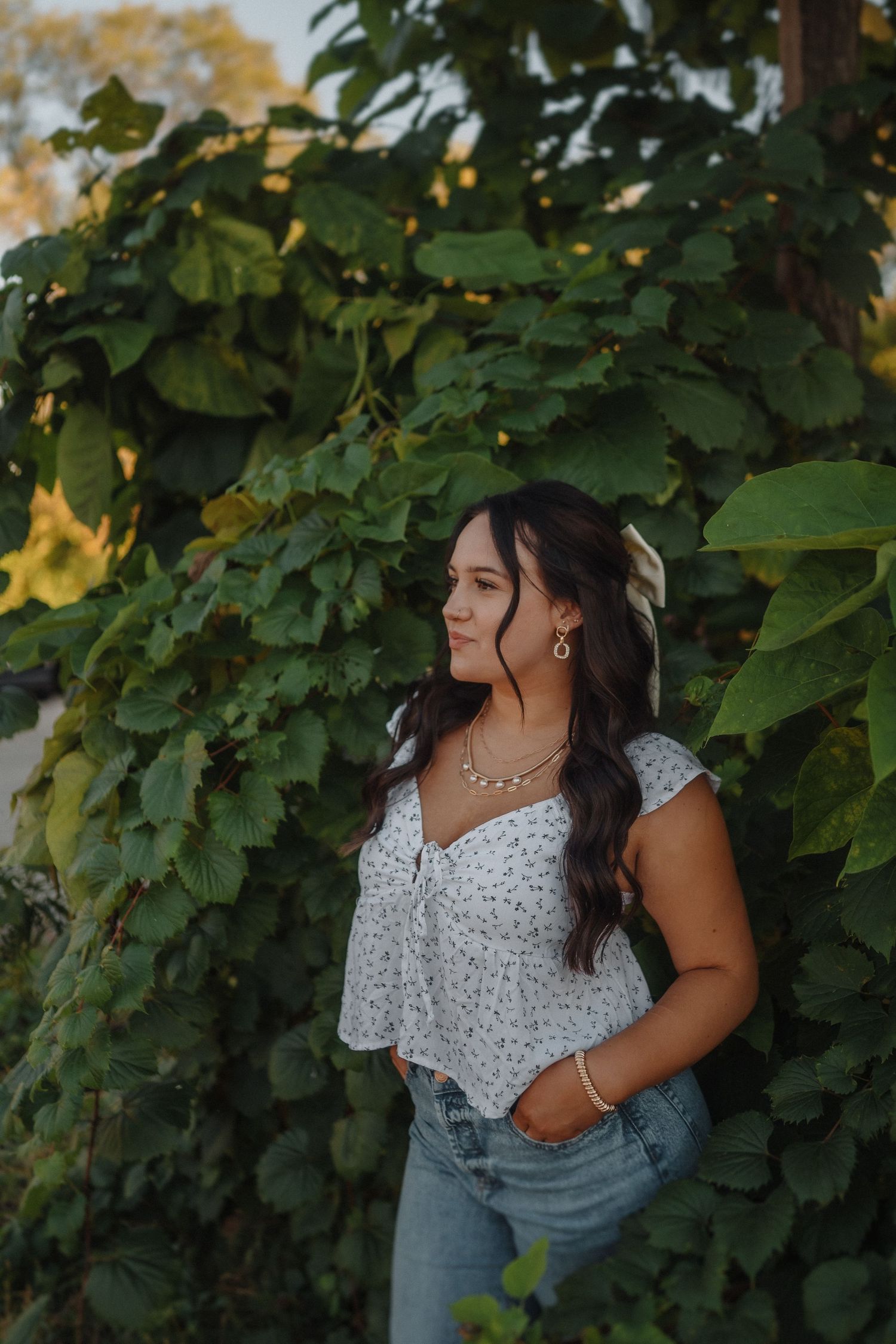 Outdoor portrait against green foliage wearing a floral crop top and jeans at golden hour.