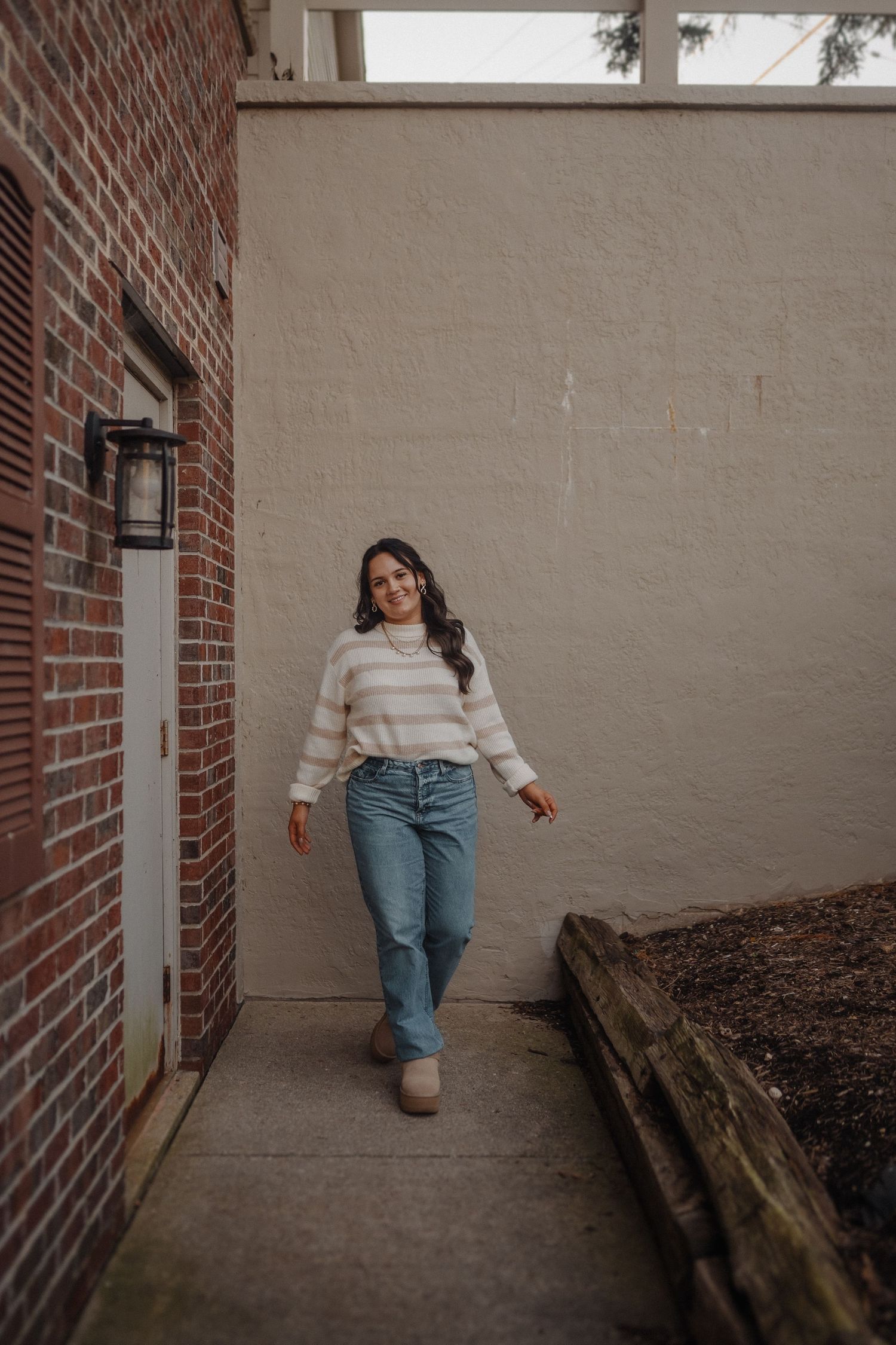 Casual lifestyle portrait against brick and concrete wall wearing striped sweater and jeans.