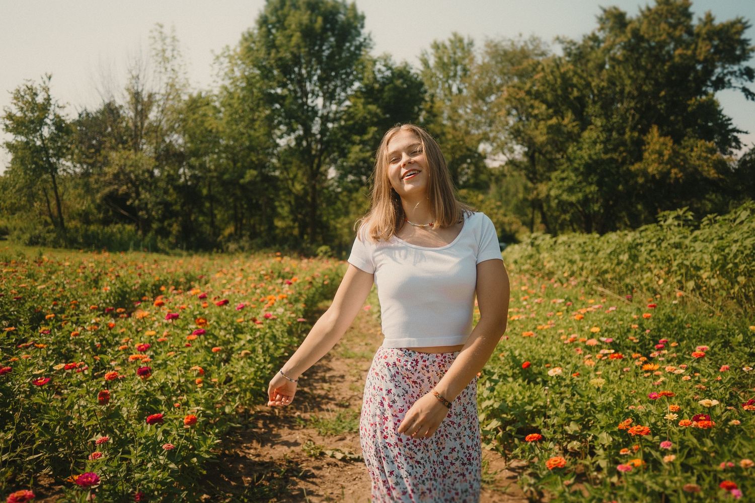 A sunny outdoor portrait in a wildflower field with orange blooms and green trees in the background.