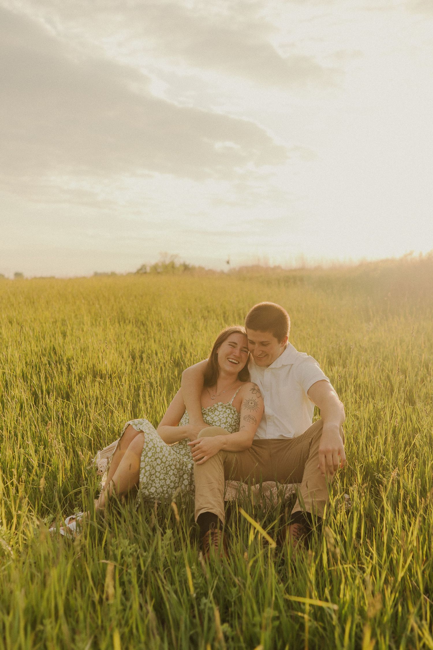 A romantic couple embraces in tall grass during a golden sunset.