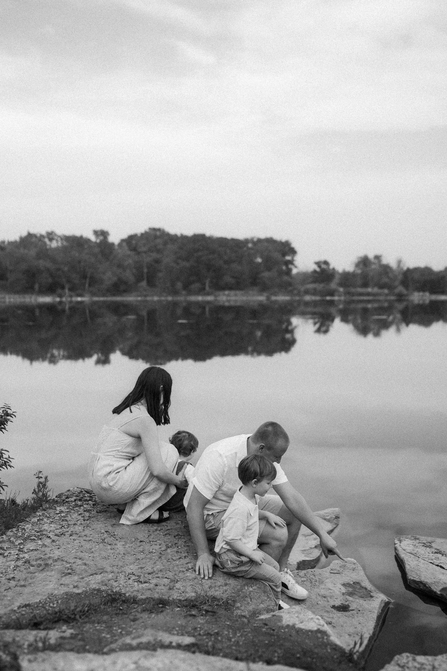 Children climb on a lakeside embankment while exploring the waterfront in a black and white photograph.
