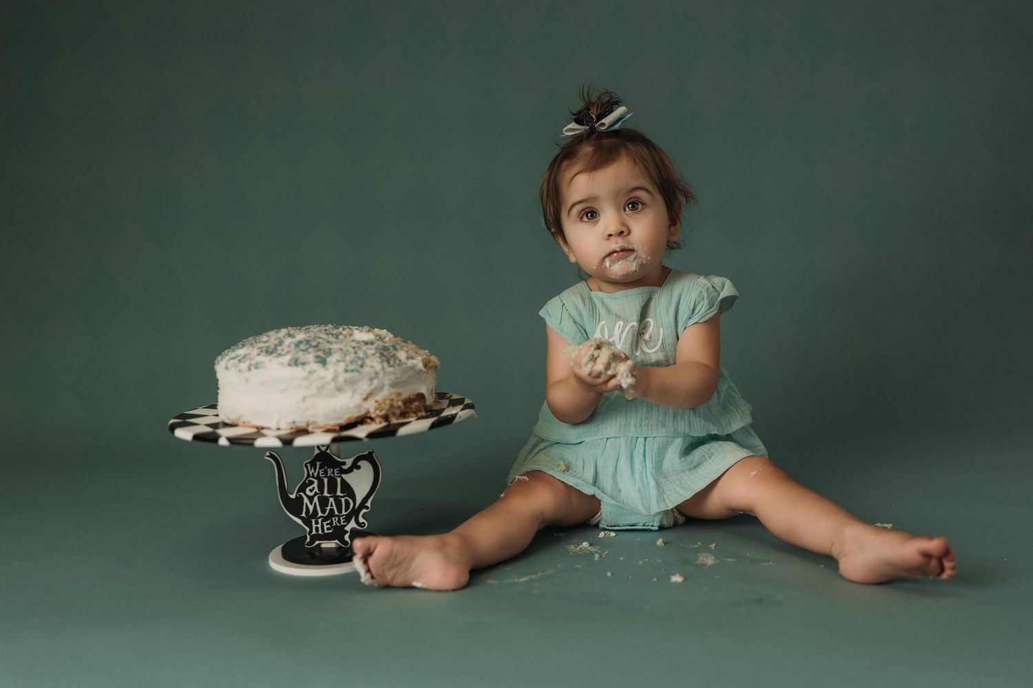 Professional birthday photo featuring a white cake on striped stand against emerald background.