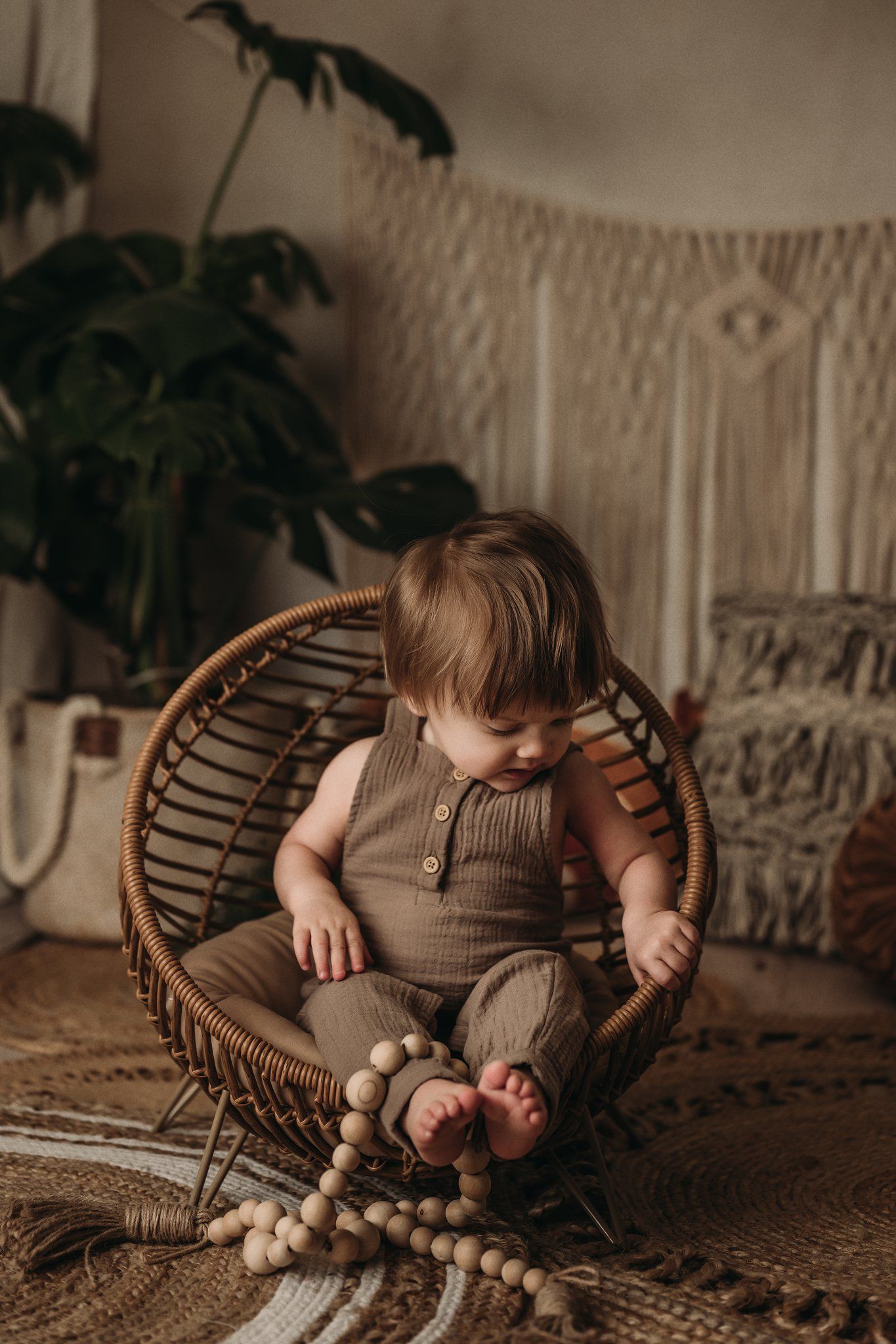 A small child relaxes in a rattan chair with wooden beads and macrame wall hangings in the background.