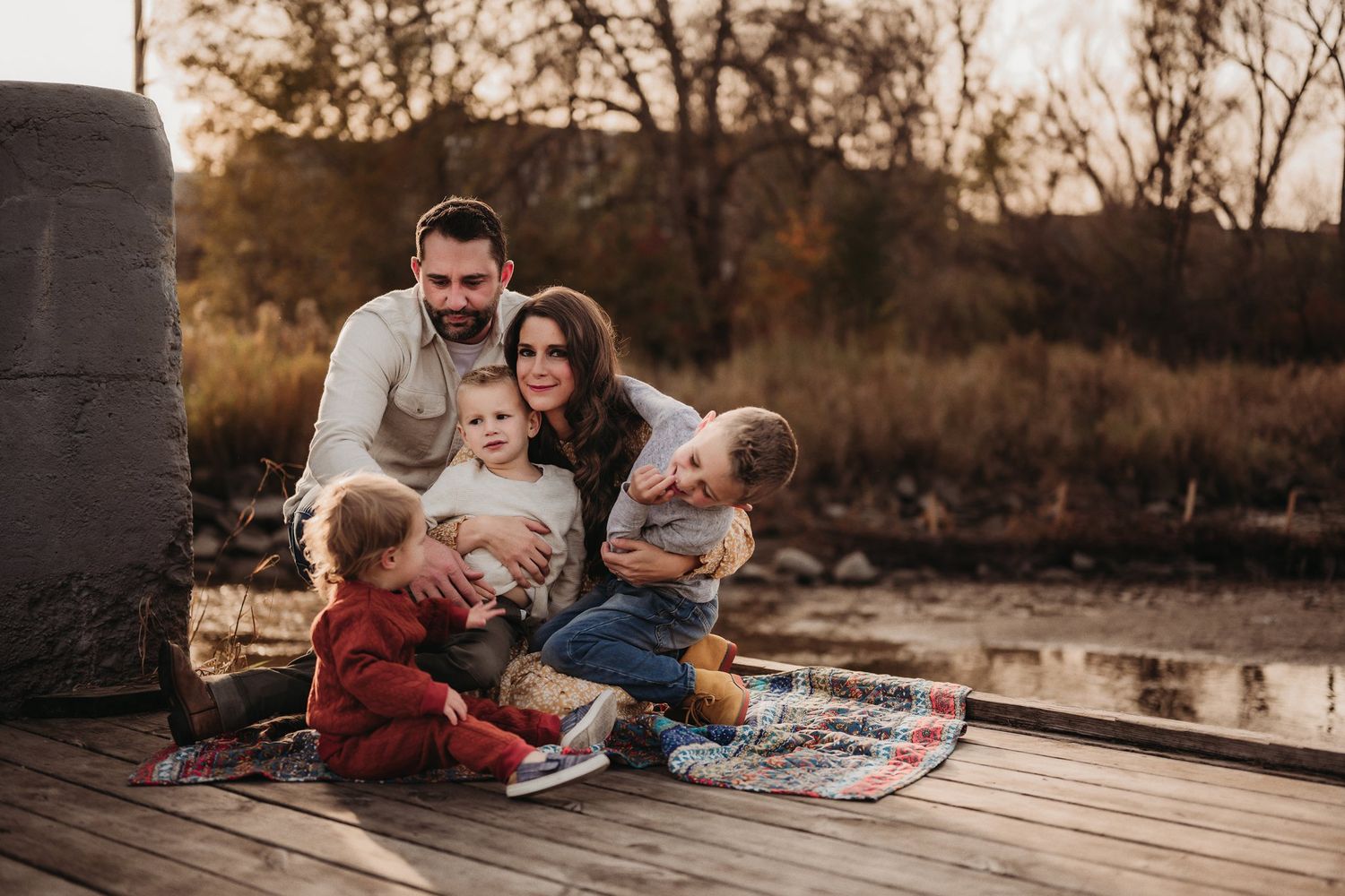 Family relaxing together on a wooden deck at sunset with a patterned blanket.
