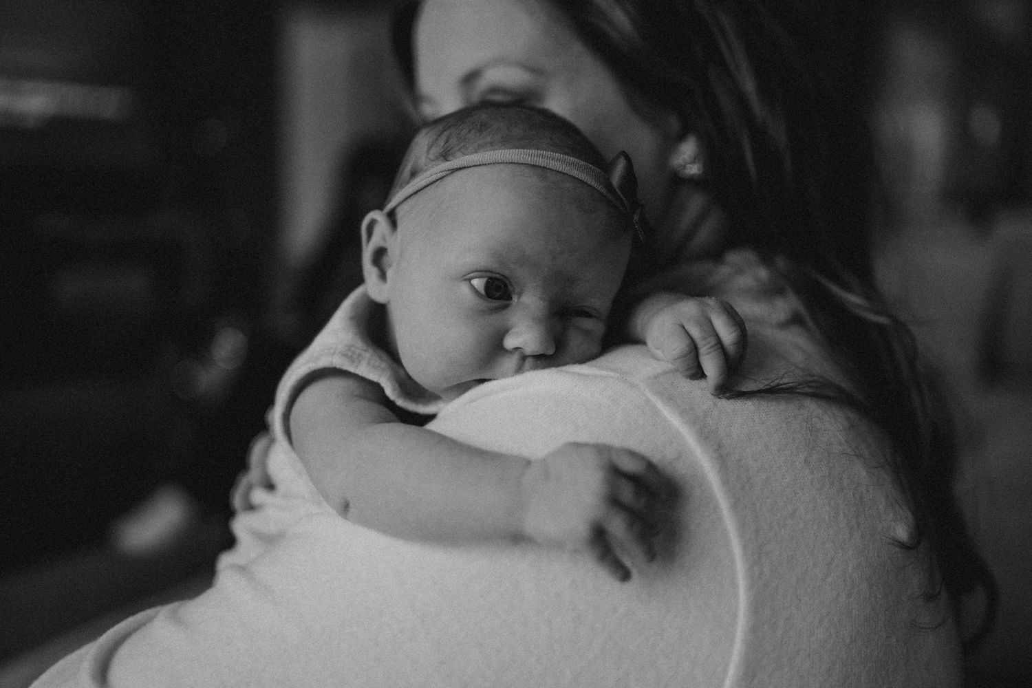Black and white portrait of baby in headband resting on shoulder.