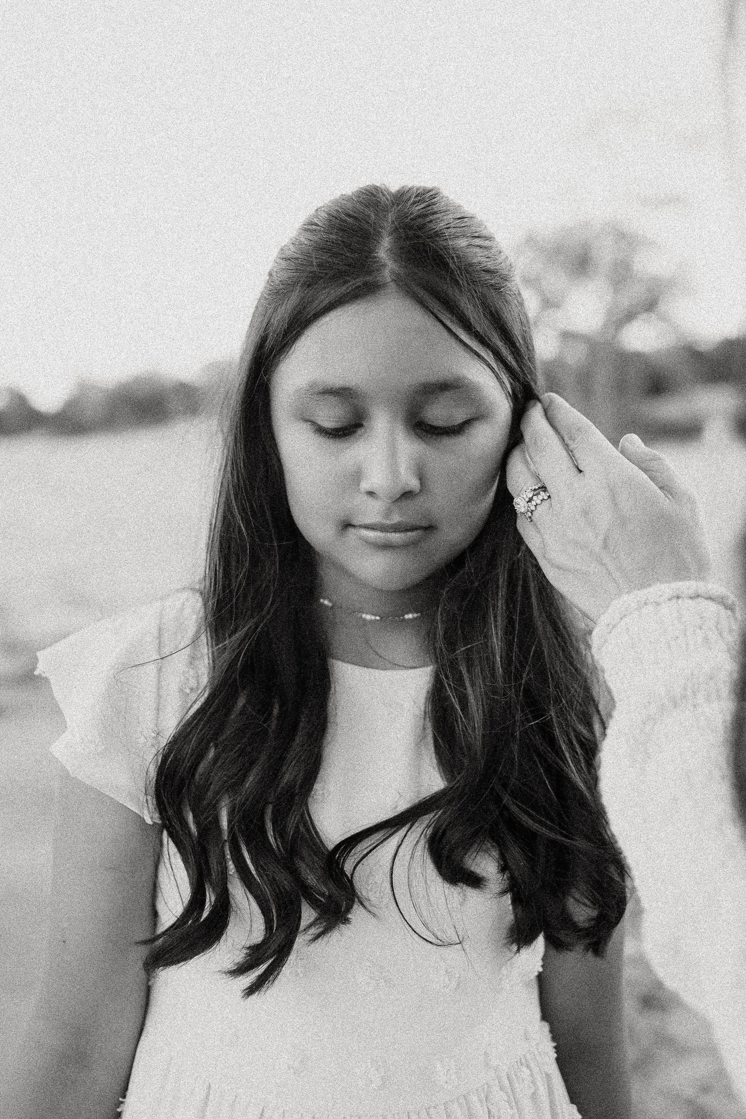 Black and white portrait of young girl with eyes closed as hand gently touches her hair.