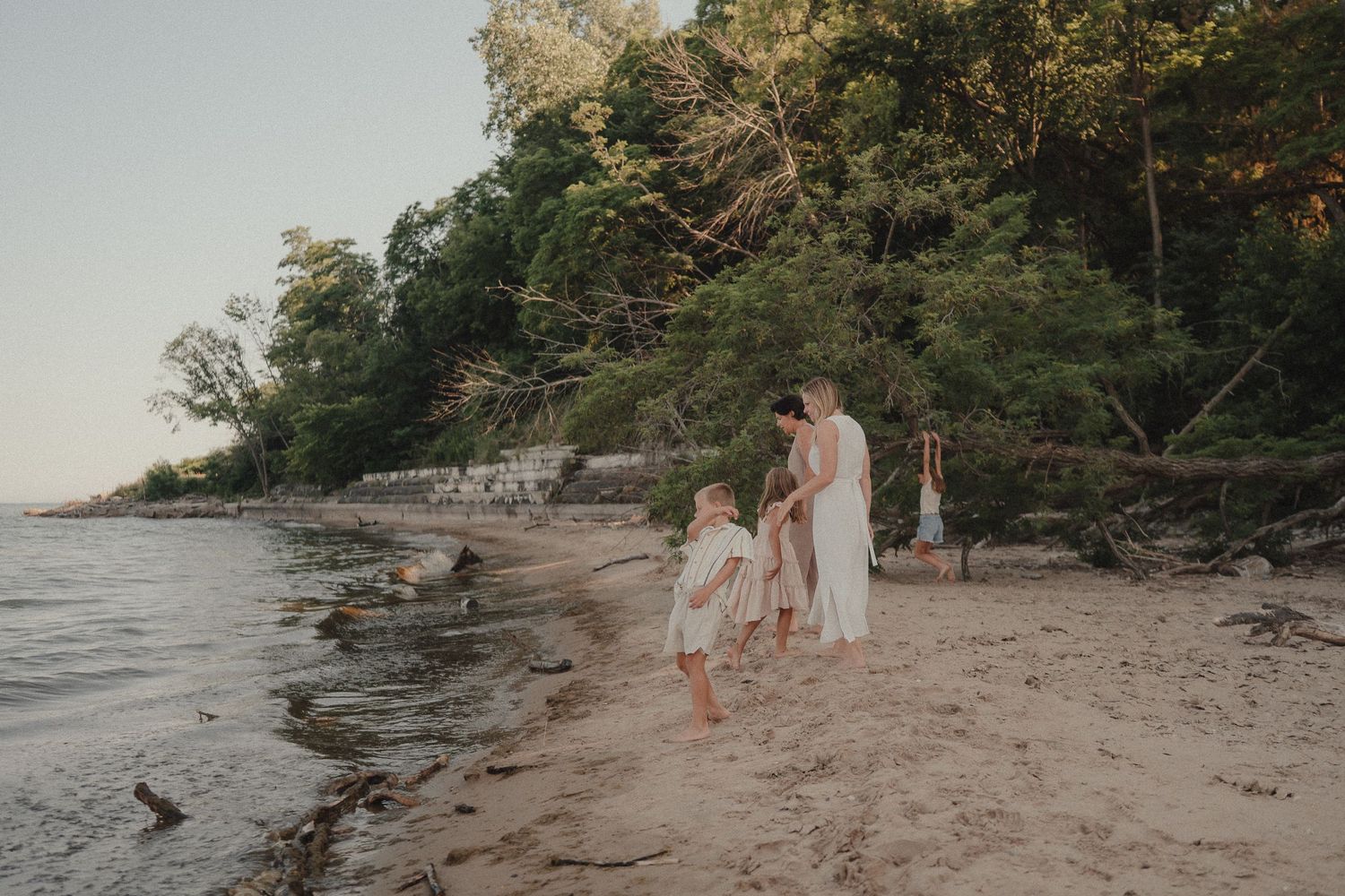 Family walking along a sandy beach at sunset, surrounded by lush green trees and calm water.