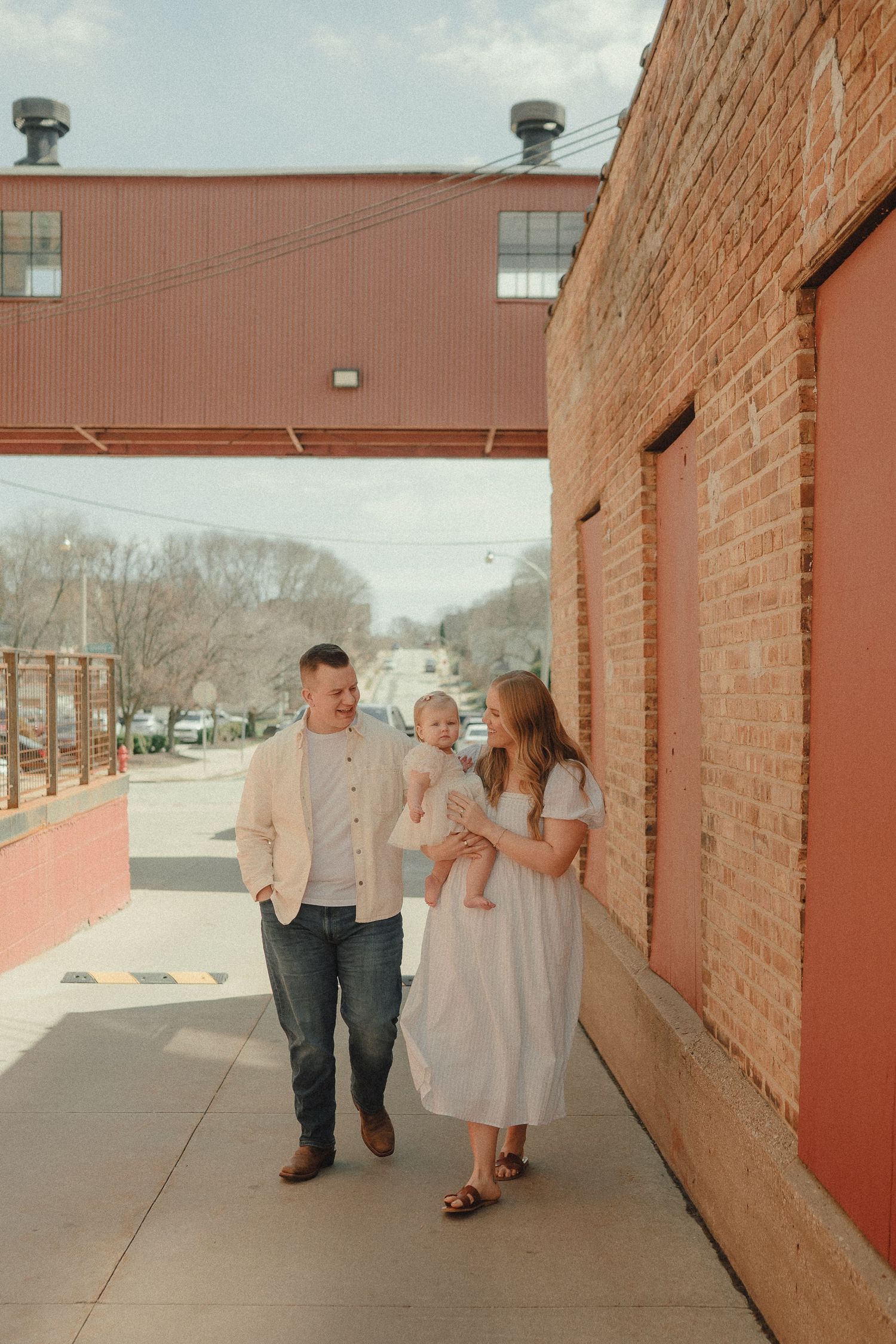 Young family walking together along a brick building sidewalk on a sunny spring day.