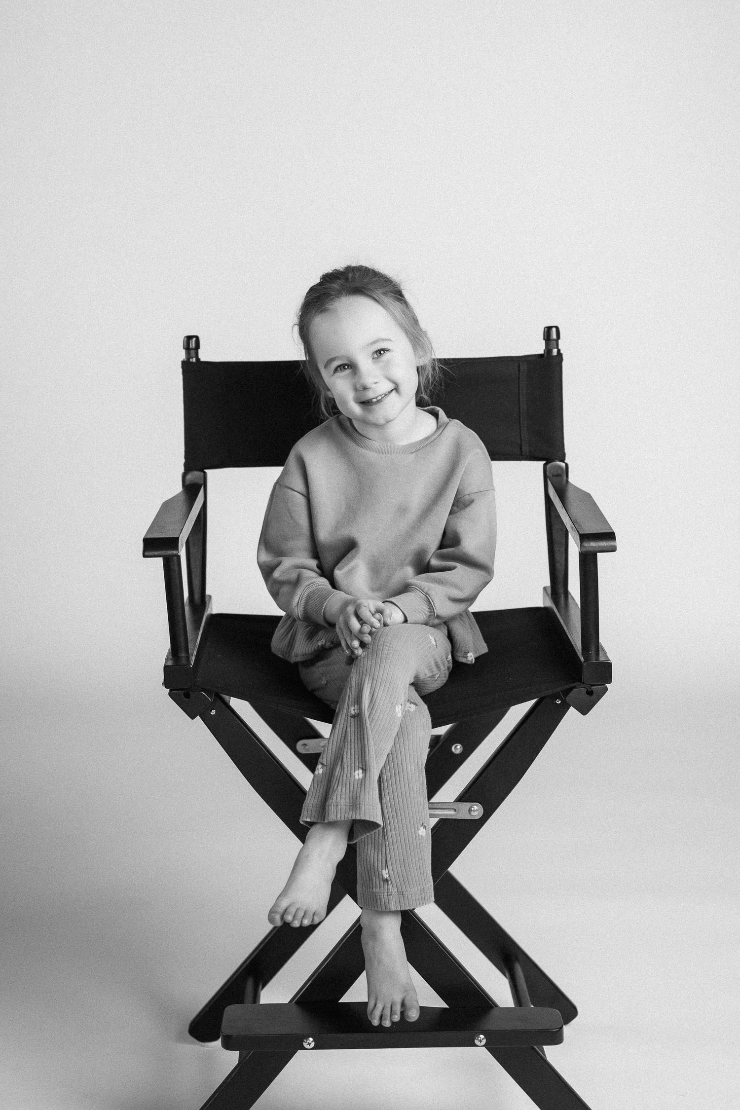Black and white photo sequence showing joyful poses on a director's chair against a white backdrop.