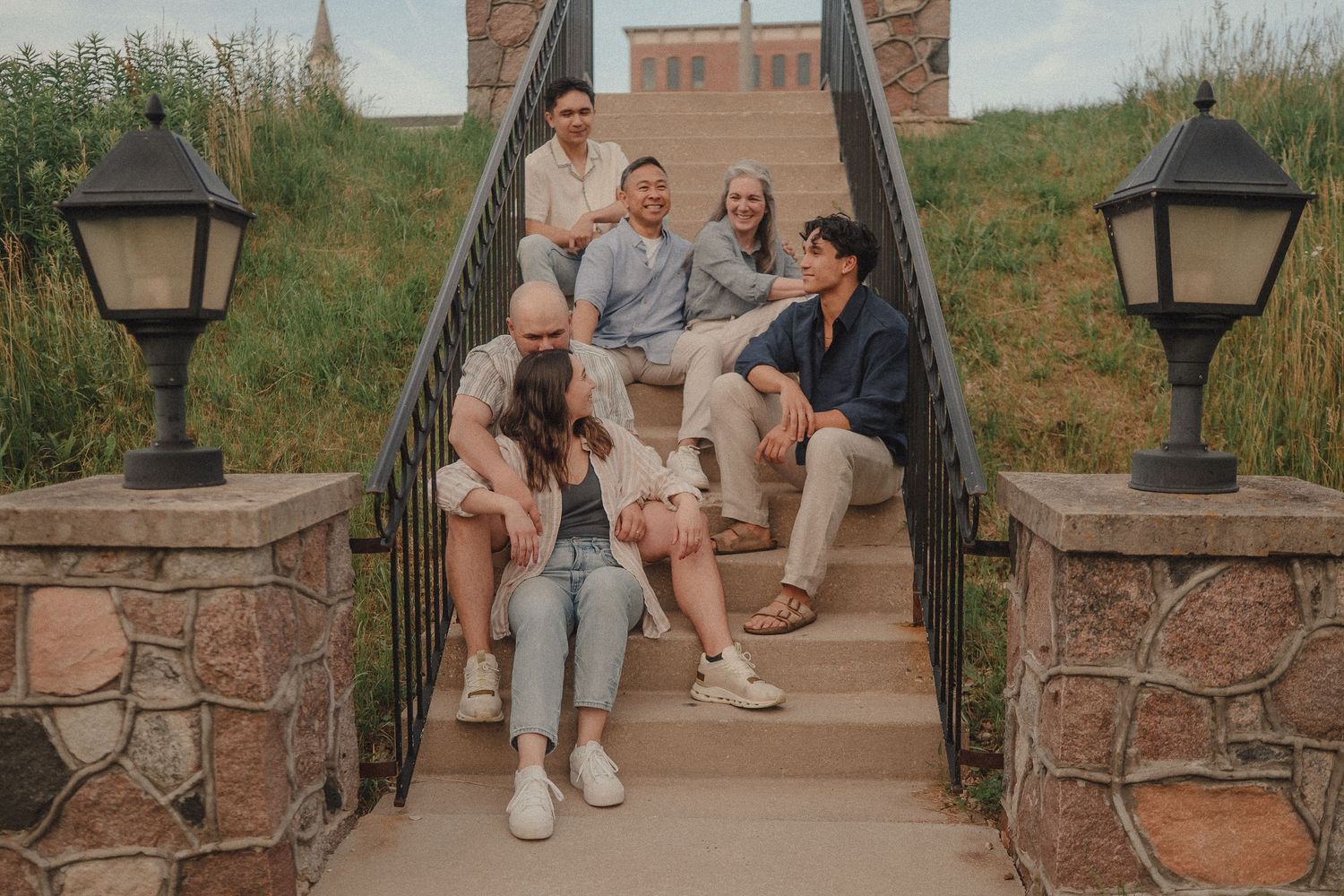 Group of five friends laughing and posing on stone steps outdoors with lamp posts and green hills.