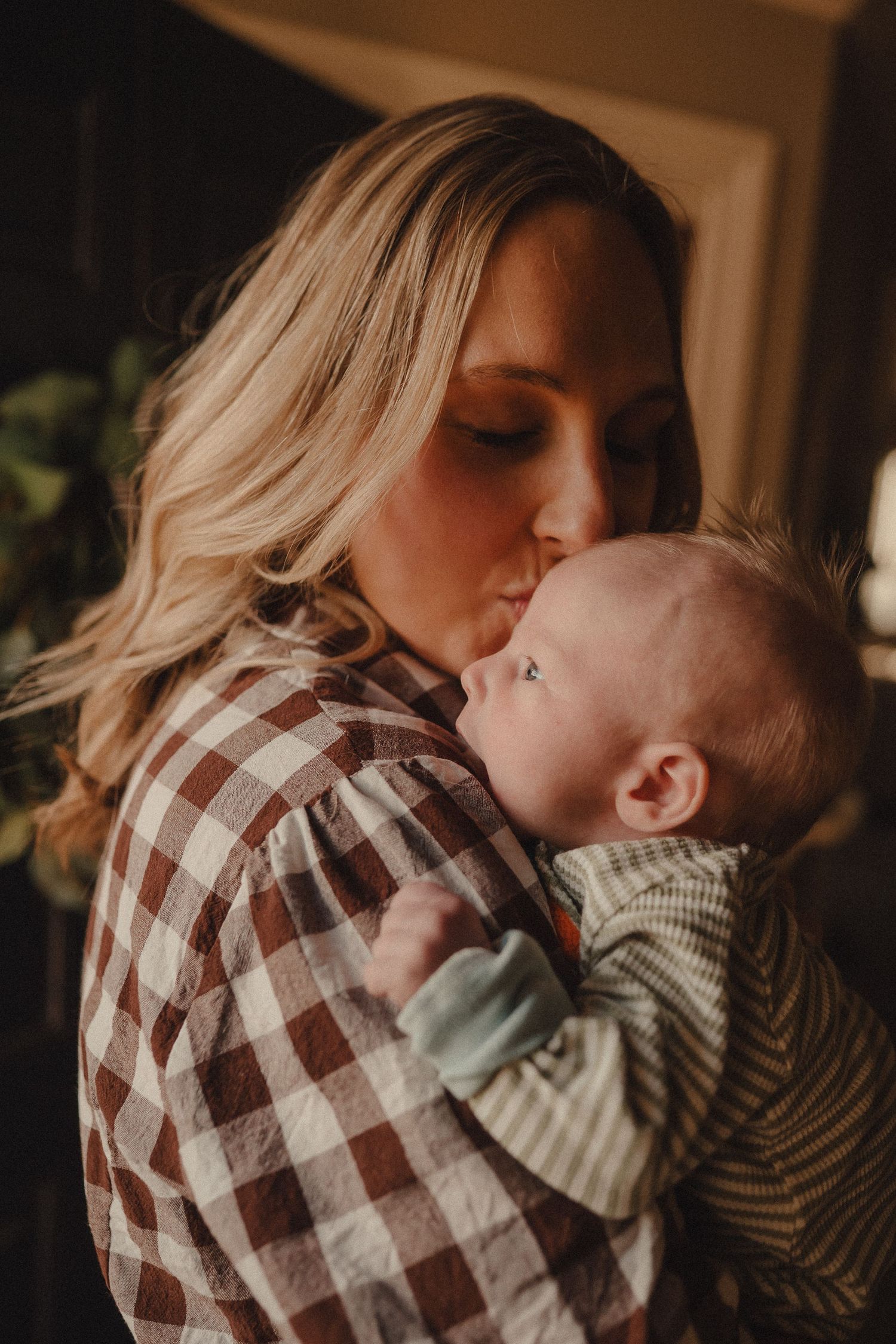 A mother tenderly kisses her newborn baby while holding him close in a warm, dimly lit room.