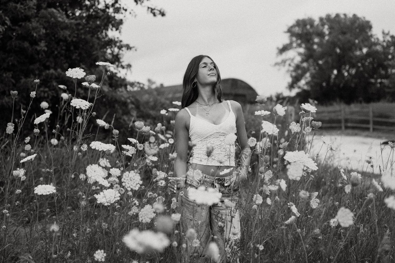 Woman standing in wildflower field with eyes closed, serene black and white portrait photography.