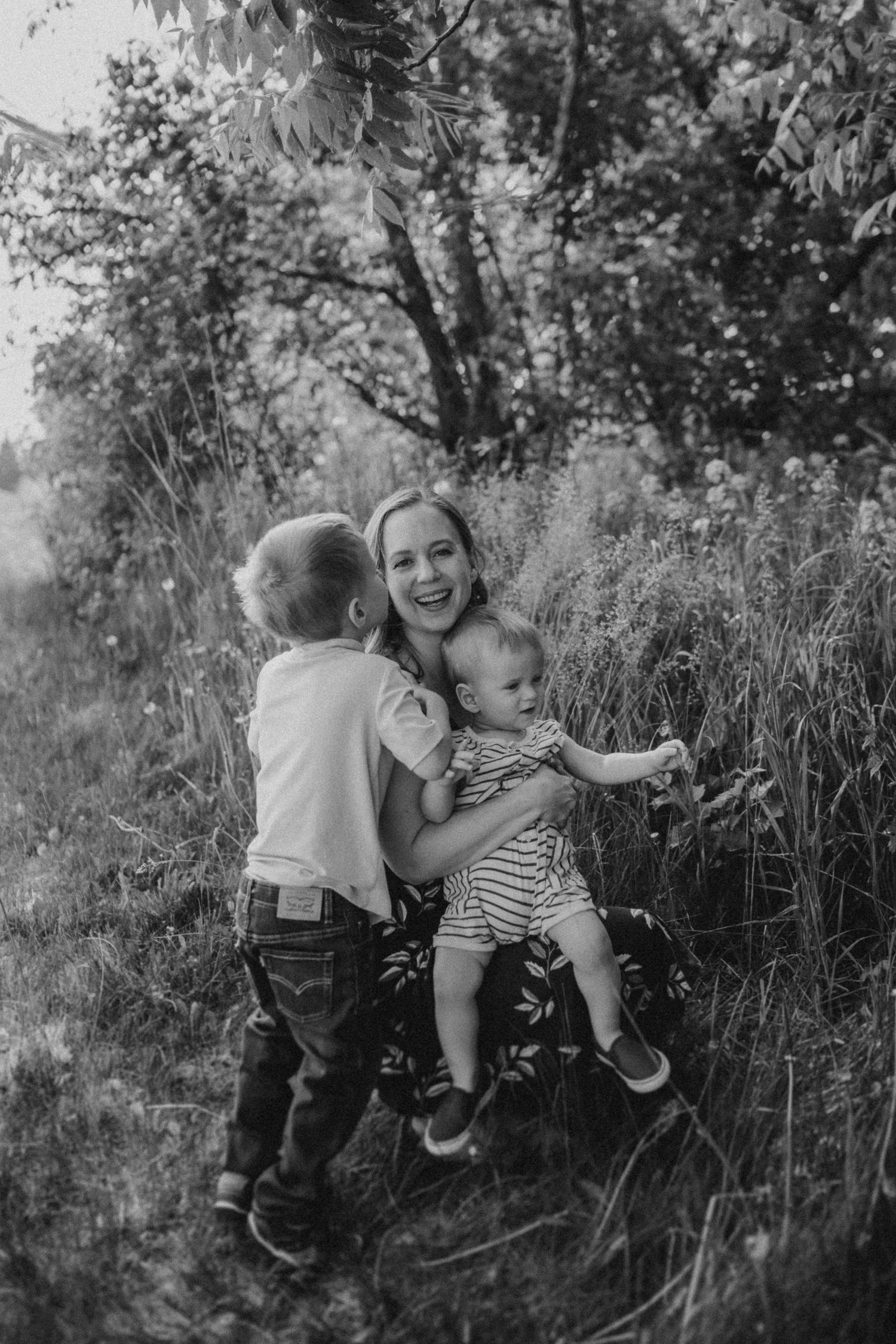 A candid black and white family moment captured in tall grass and wildflowers.