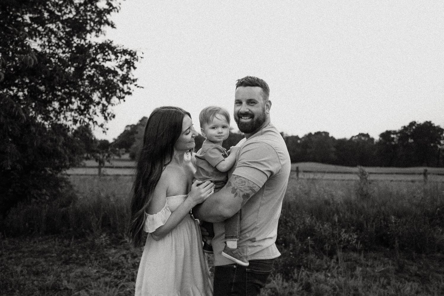 An intimate black and white family portrait in a rustic outdoor setting.