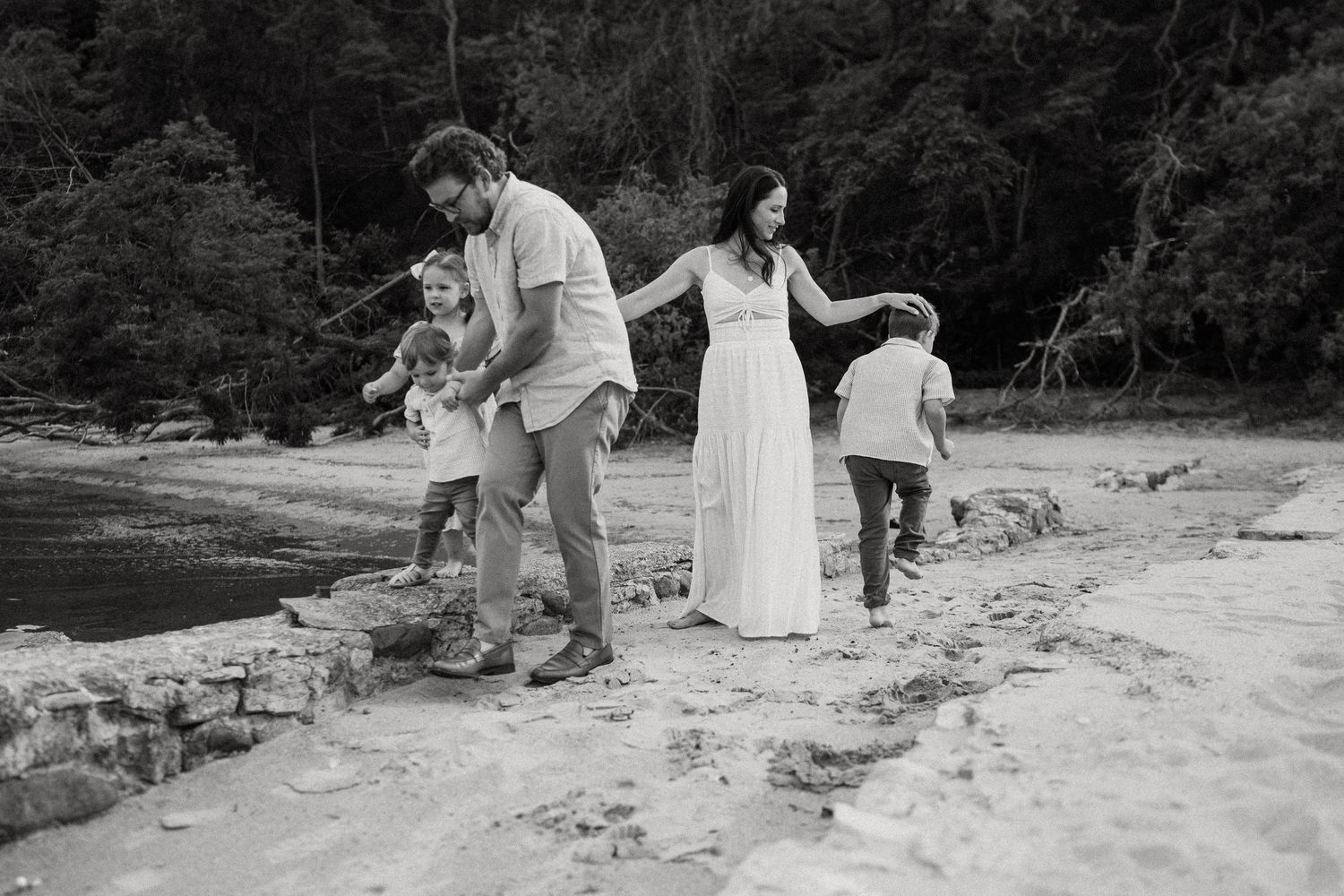 A family walks together along rocky coastal terrain while wearing white outfits.