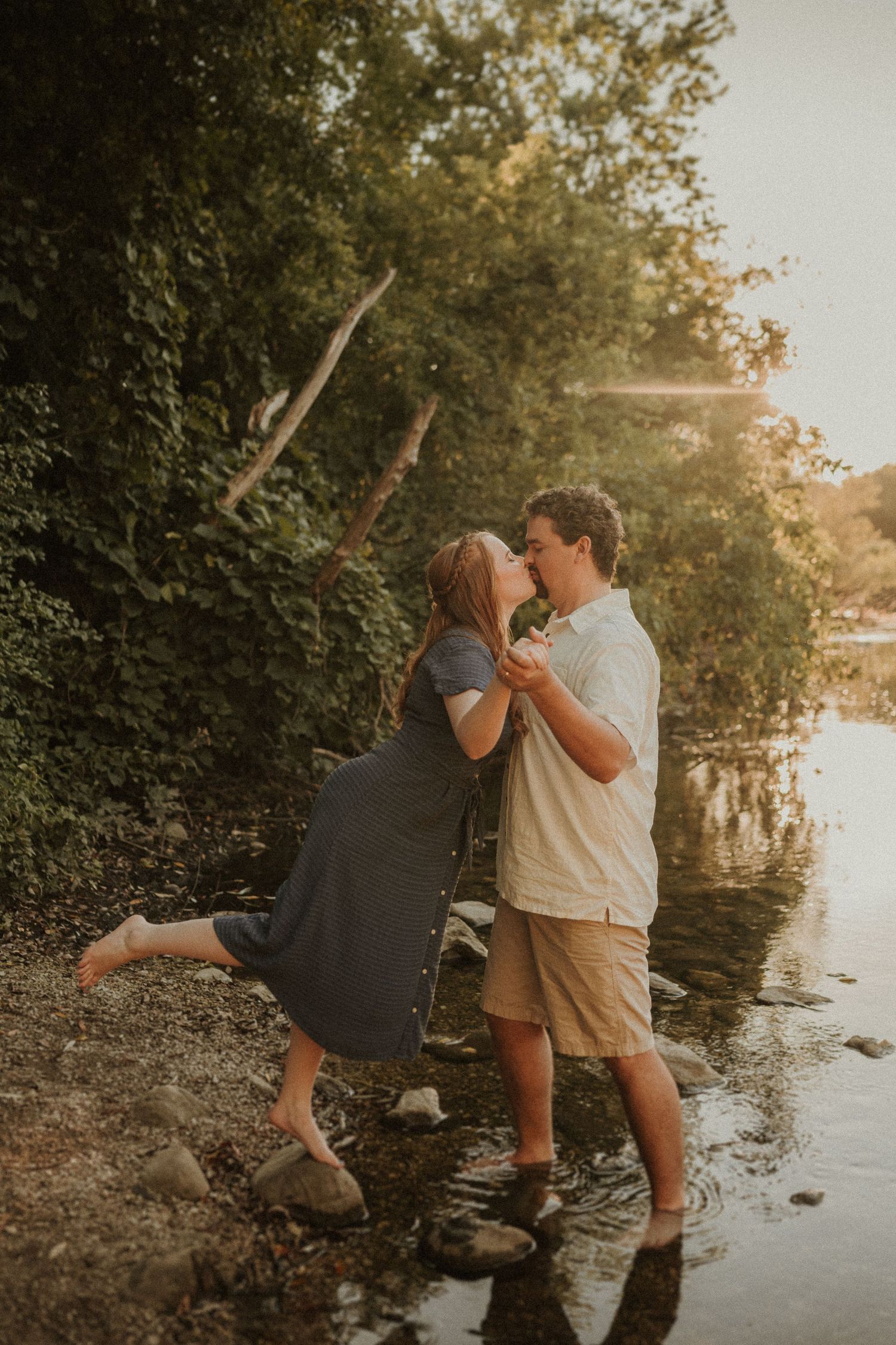 Romantic sunset photo of a couple posing together on rocks by the water's edge.