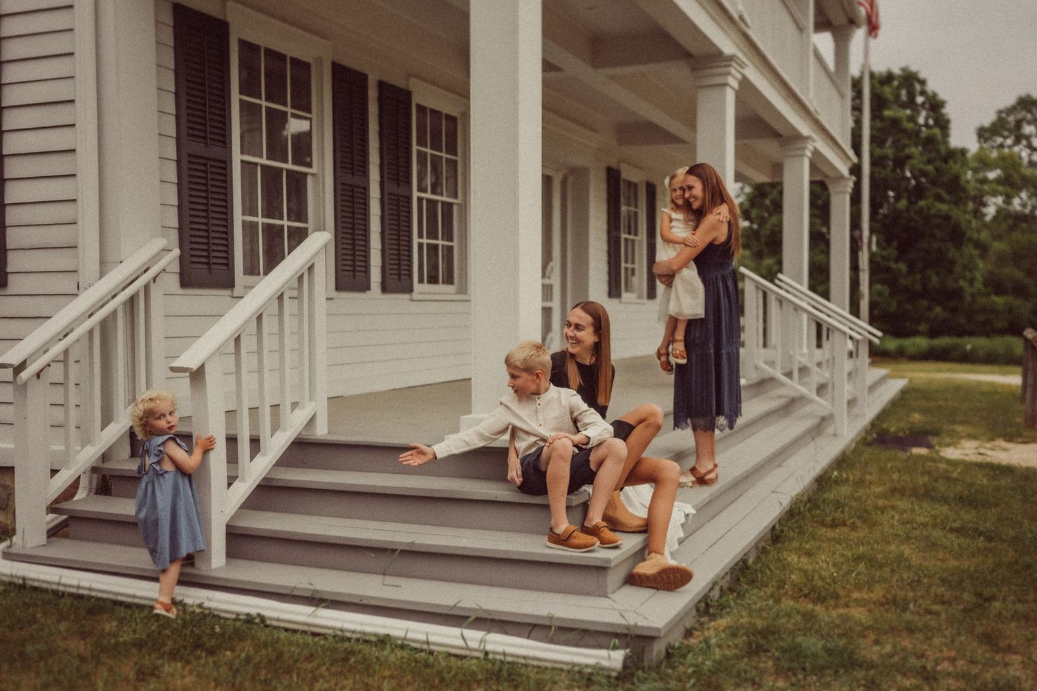 A casual family gathering on white farmhouse porch steps on a sunny summer day.