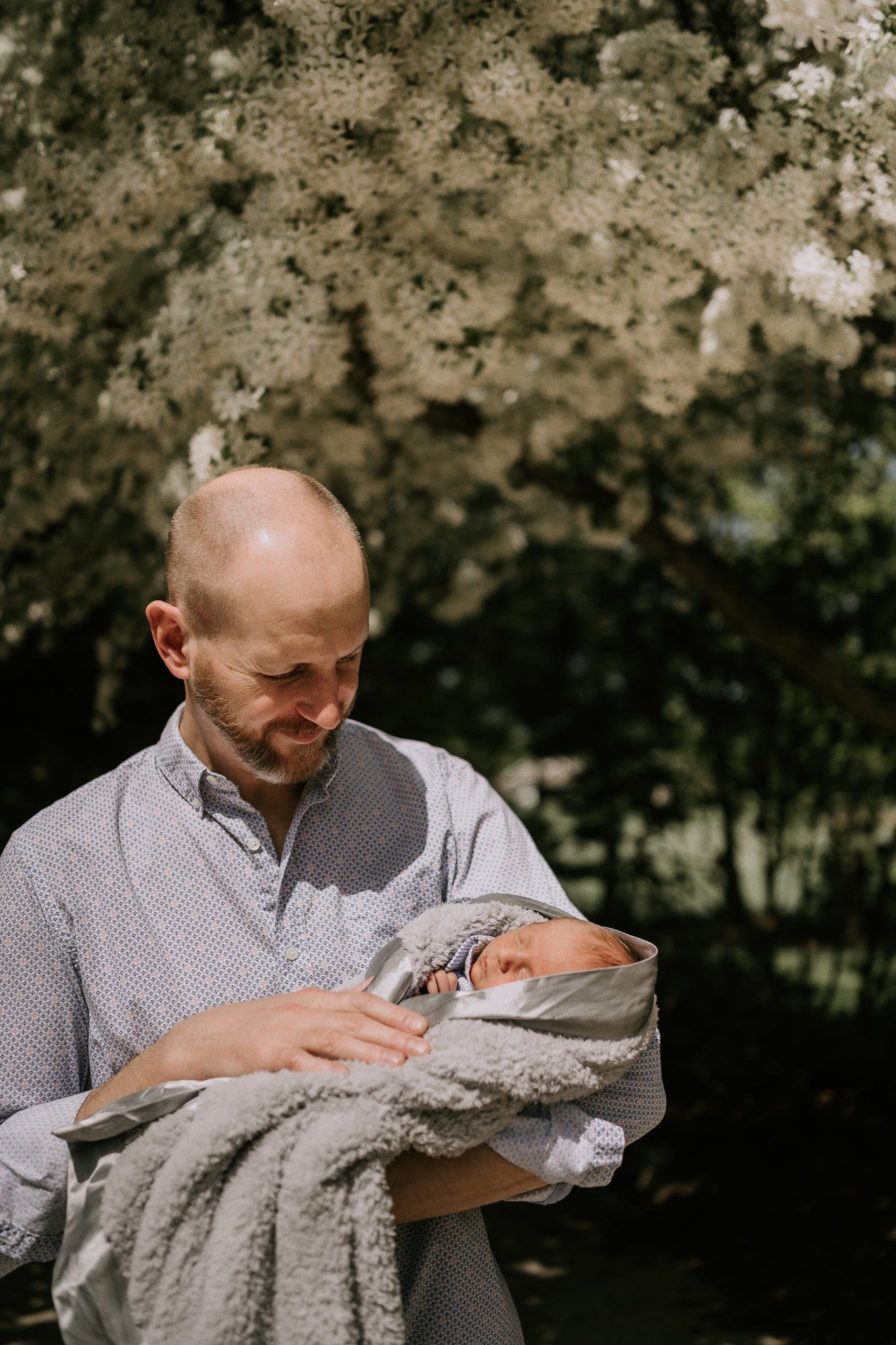 A person gazes lovingly at a swaddled newborn baby under blooming spring trees.