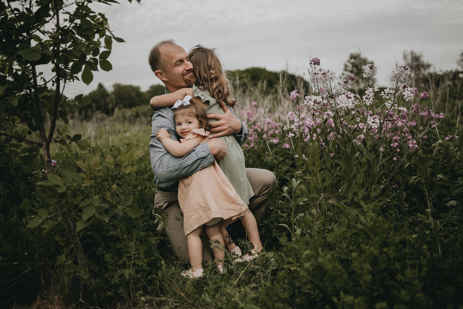 An intimate family moment captured among flowering plants during golden hour.