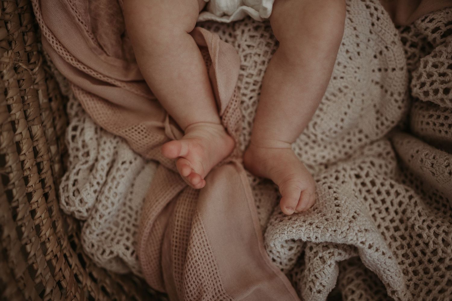 Close-up of small hands resting on woven basket with soft textured fabrics.