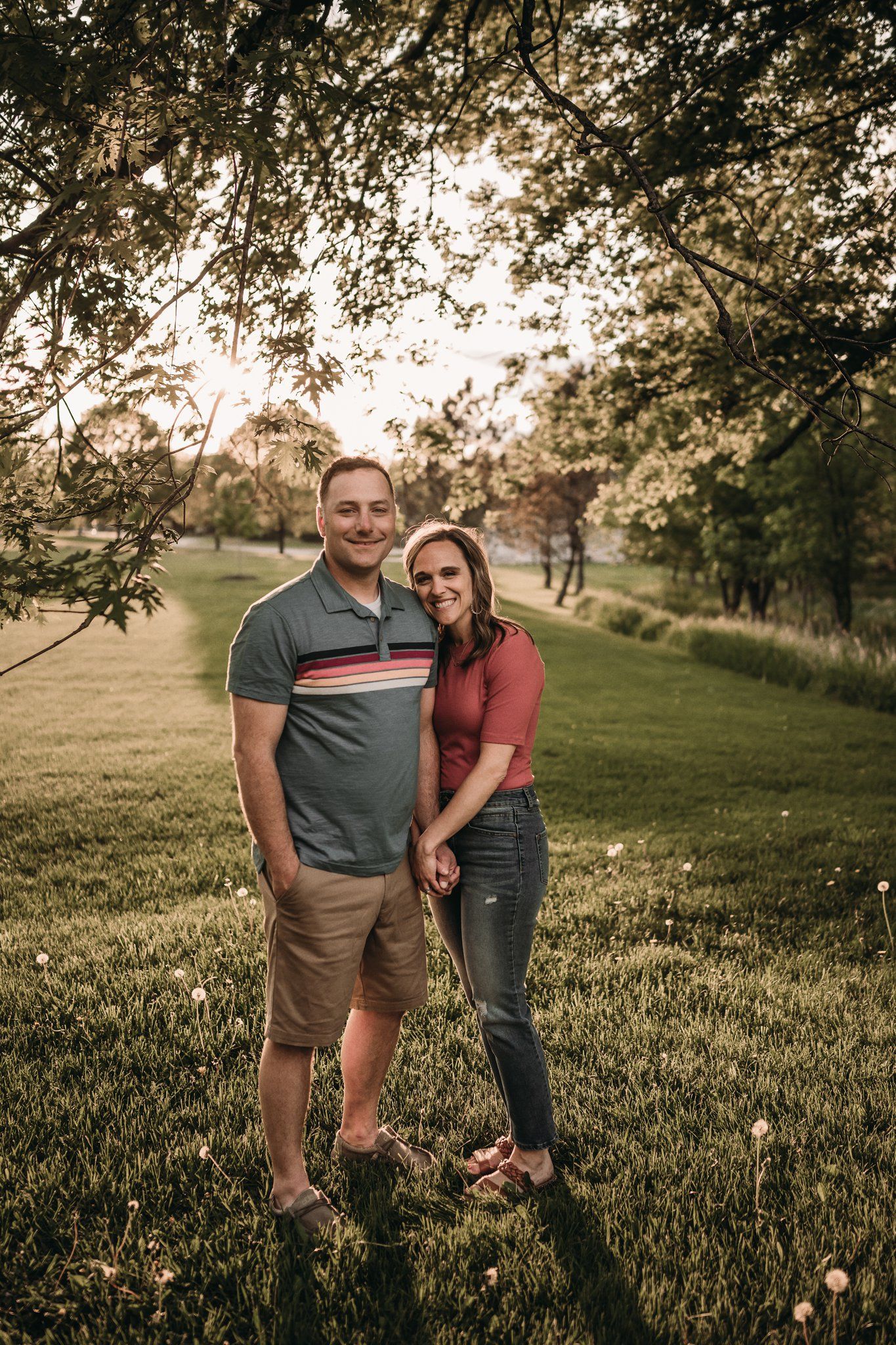 Couple poses together in a scenic park setting during golden hour.