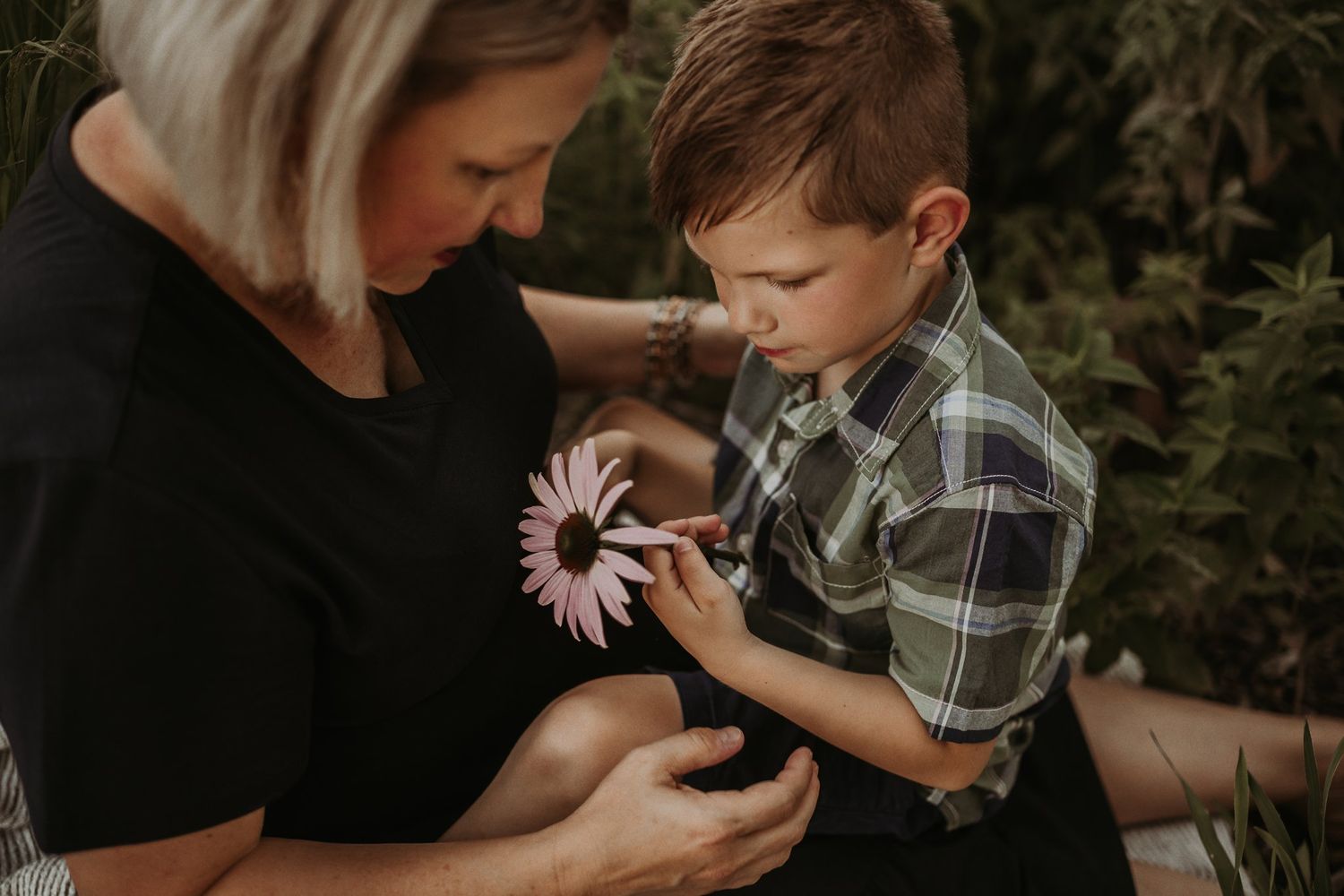 A touching moment examining a pink flower together in a garden setting.