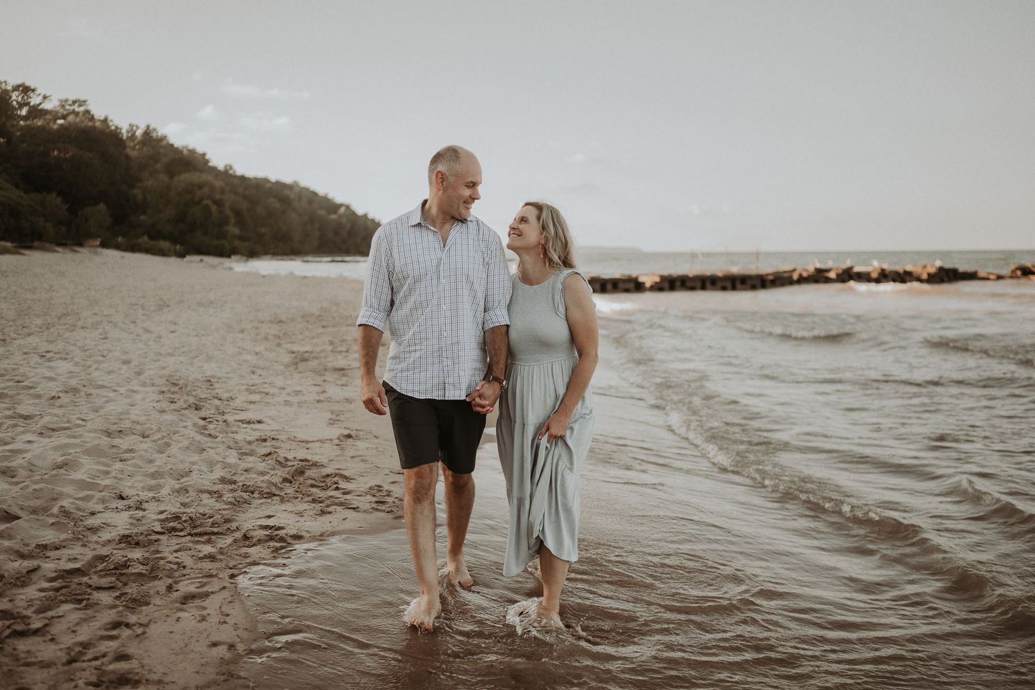 Couple walking hand in hand along the shoreline at dusk.