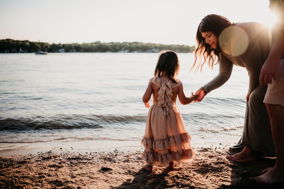 A tender moment between parent and child standing on a beach at sunset near the water's edge.