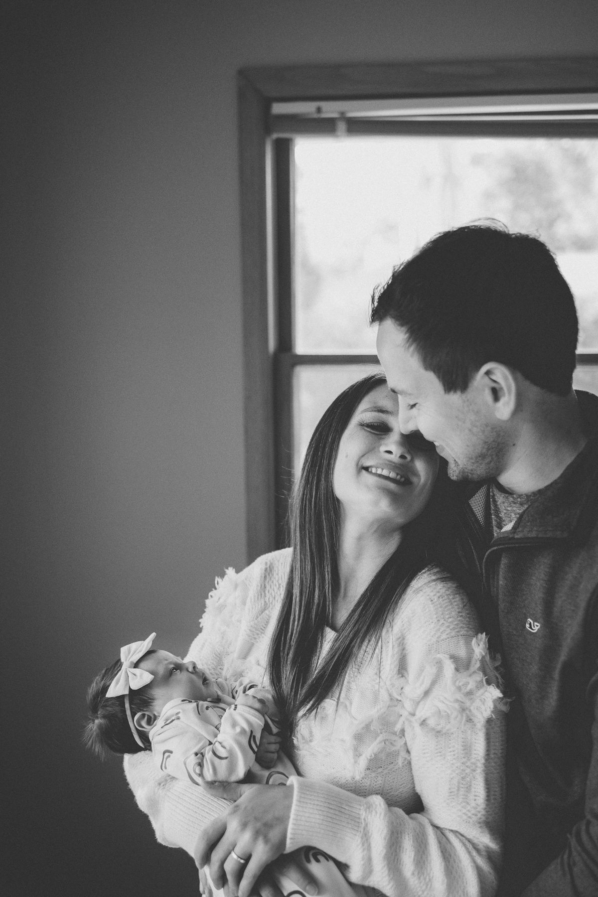 Intimate black and white portrait of a couple sharing a loving moment with their newborn.