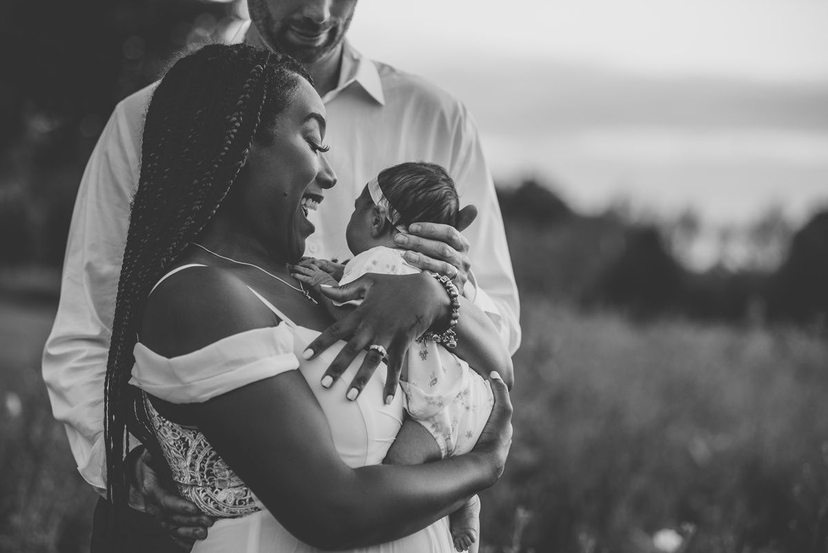 A tender black and white portrait of parents cradling their newborn outdoors.