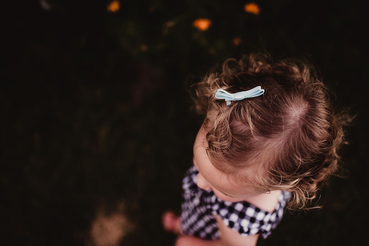 Toddler in gingham dress smelling flowers in garden.