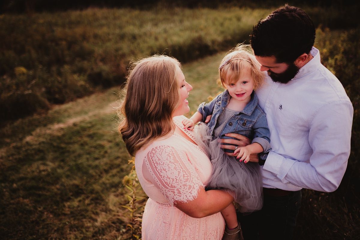 Intimate family moment captured in golden sunlight with parents embracing their child.