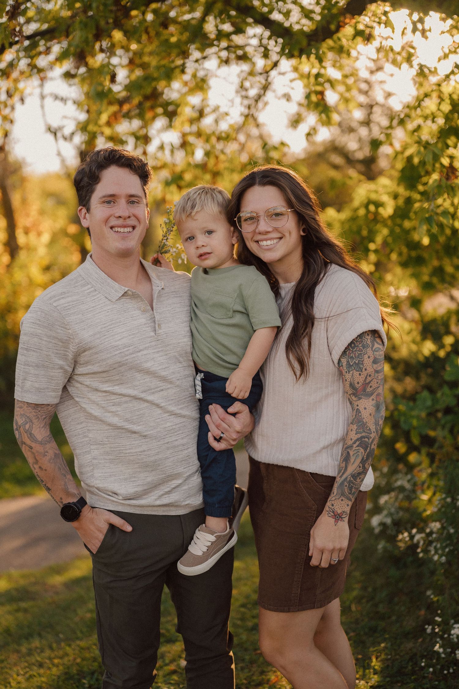 A family poses together outdoors during golden hour with autumn trees in the background.