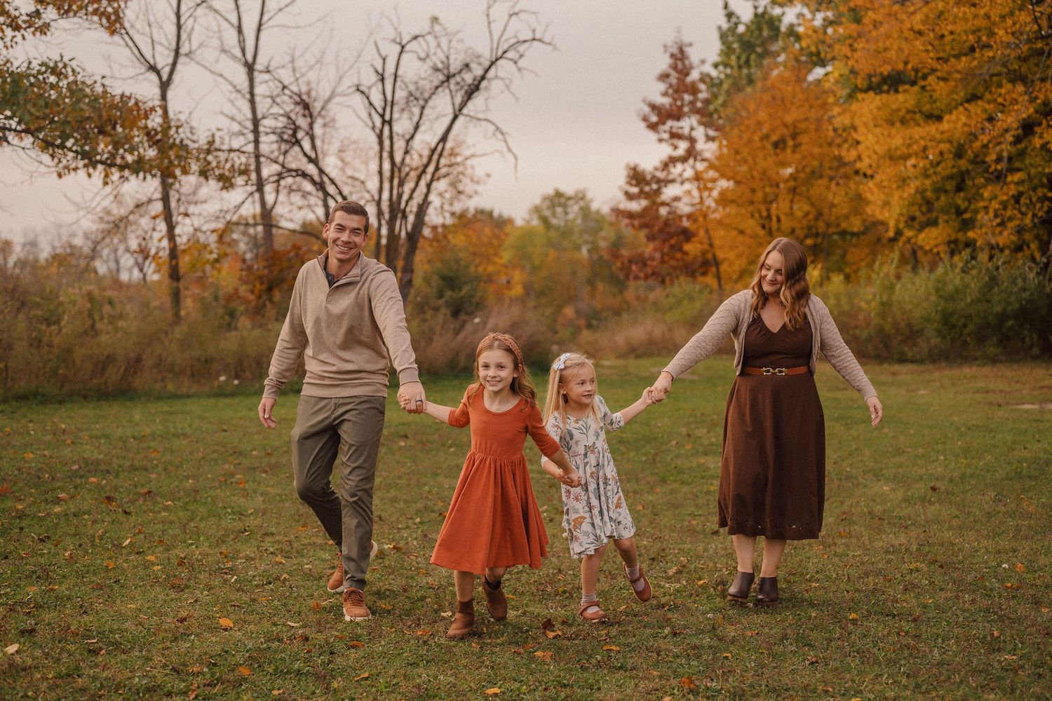 A playful family moment captured in a field with autumn trees and warm sunset lighting.