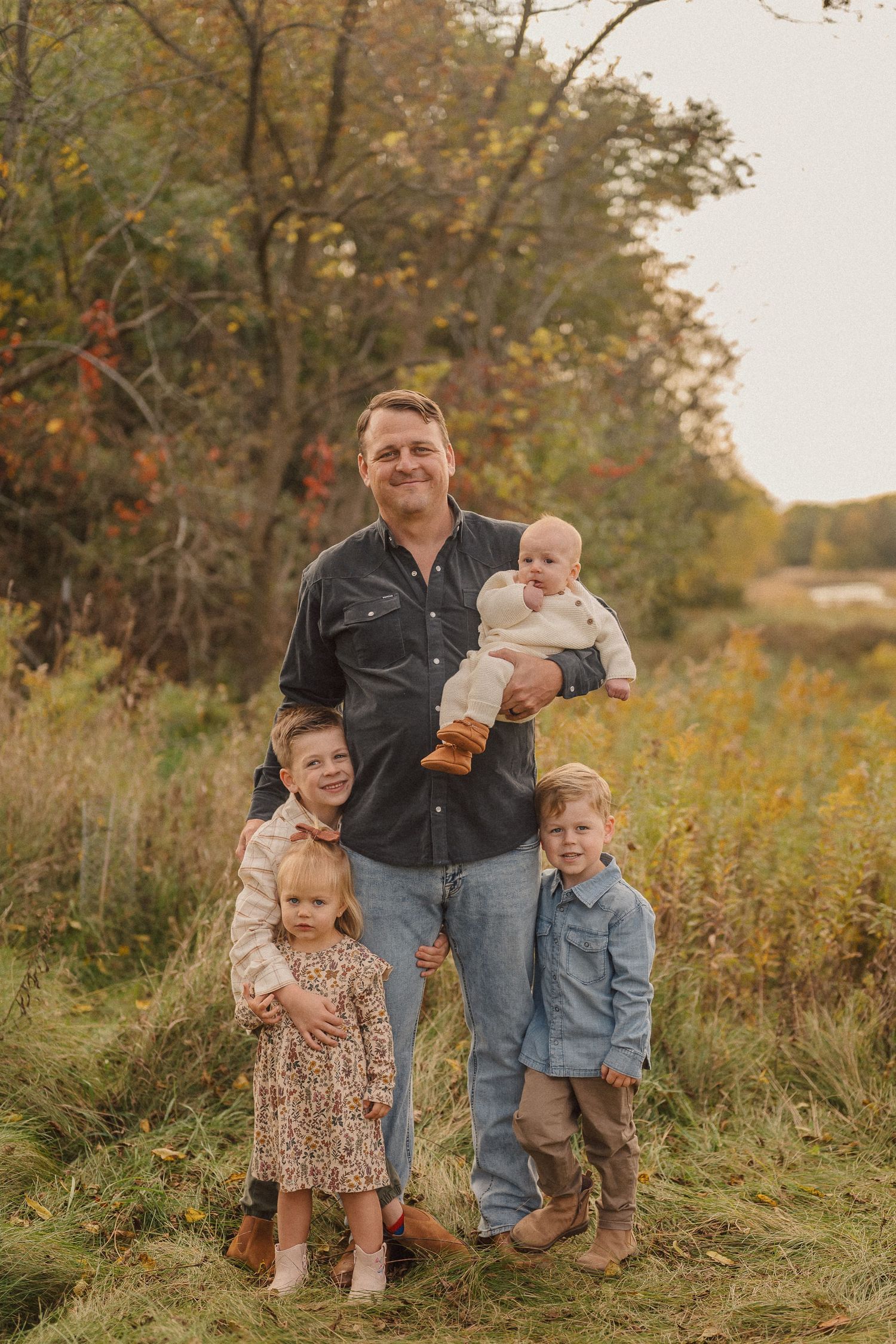 Happy family group poses together on grassy hillside during fall sunset photoshoot.