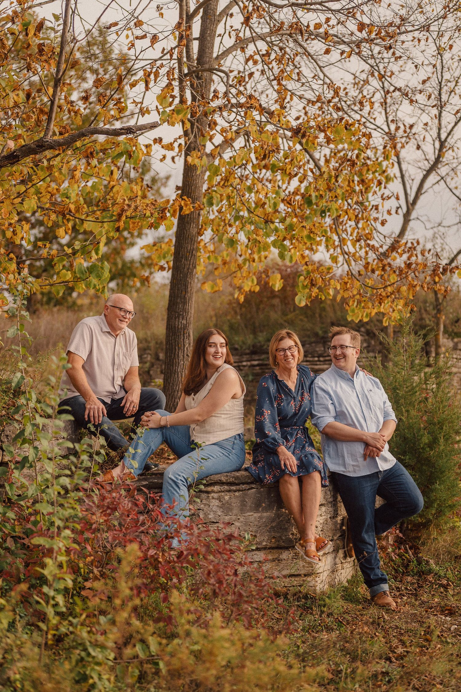People relaxing on fallen logs in a natural setting surrounded by autumn trees and red underbrush.