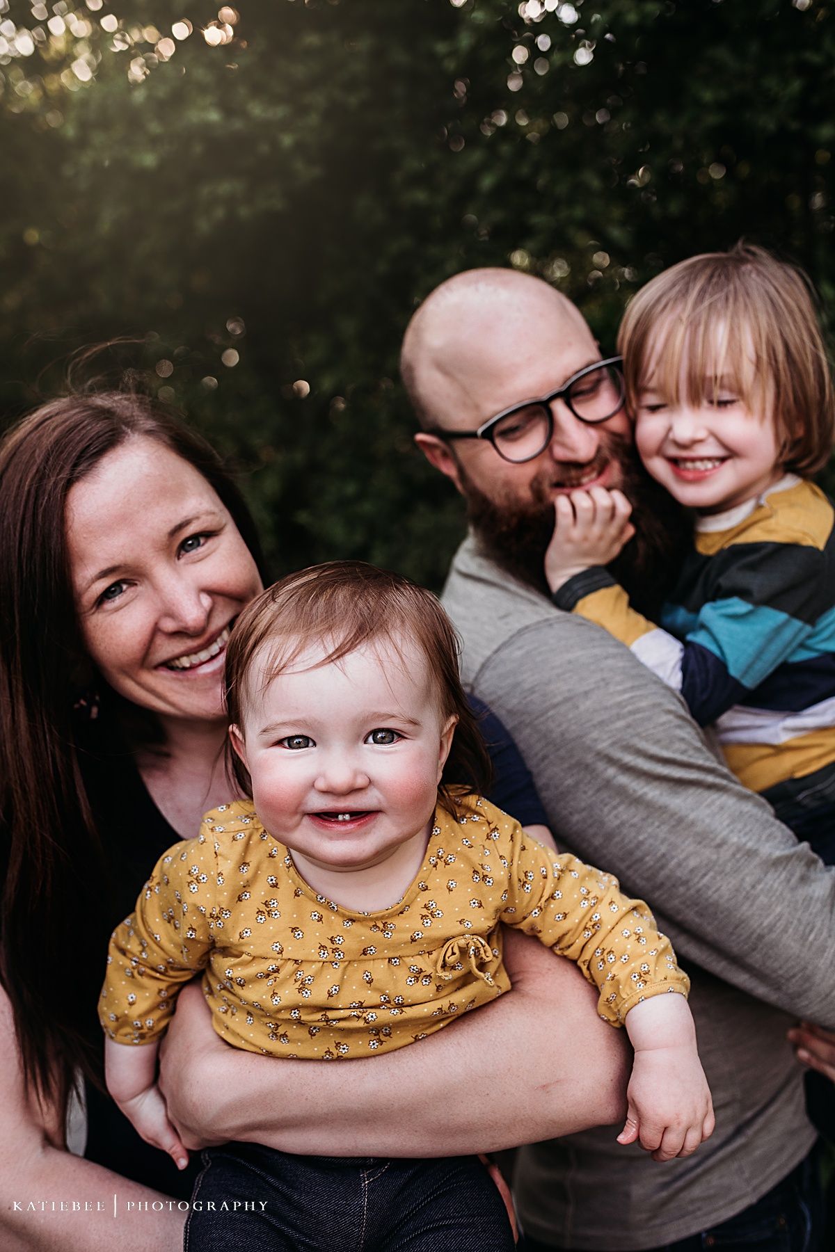 Close-up family photo with joyful expressions against a blurred natural backdrop with bokeh lights.