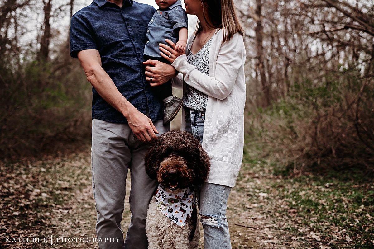 Family stands together outdoors with their curly-haired dog on autumn trail.