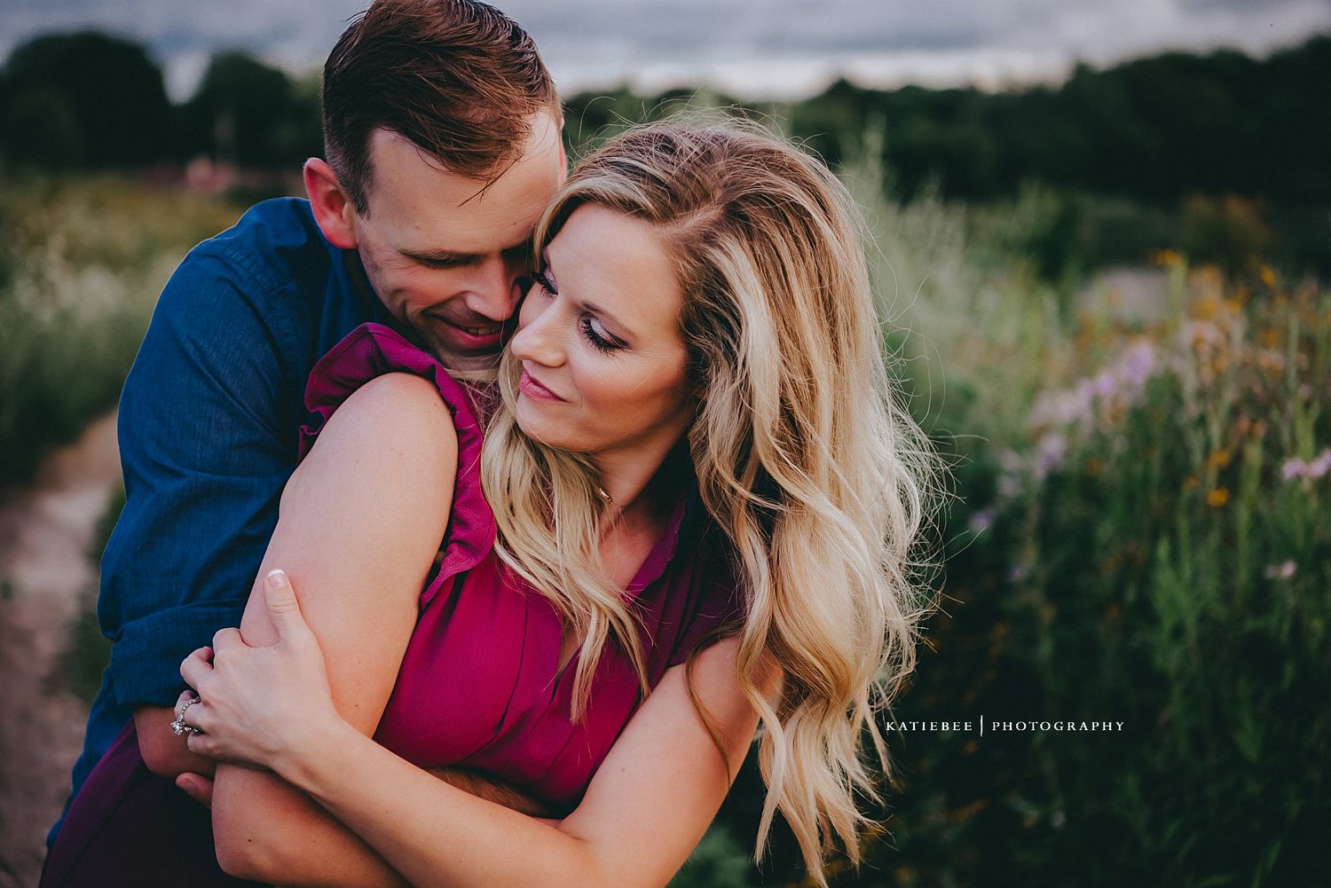 A romantic outdoor photoshoot with a couple embracing in a field at sunset wearing blue and burgundy.