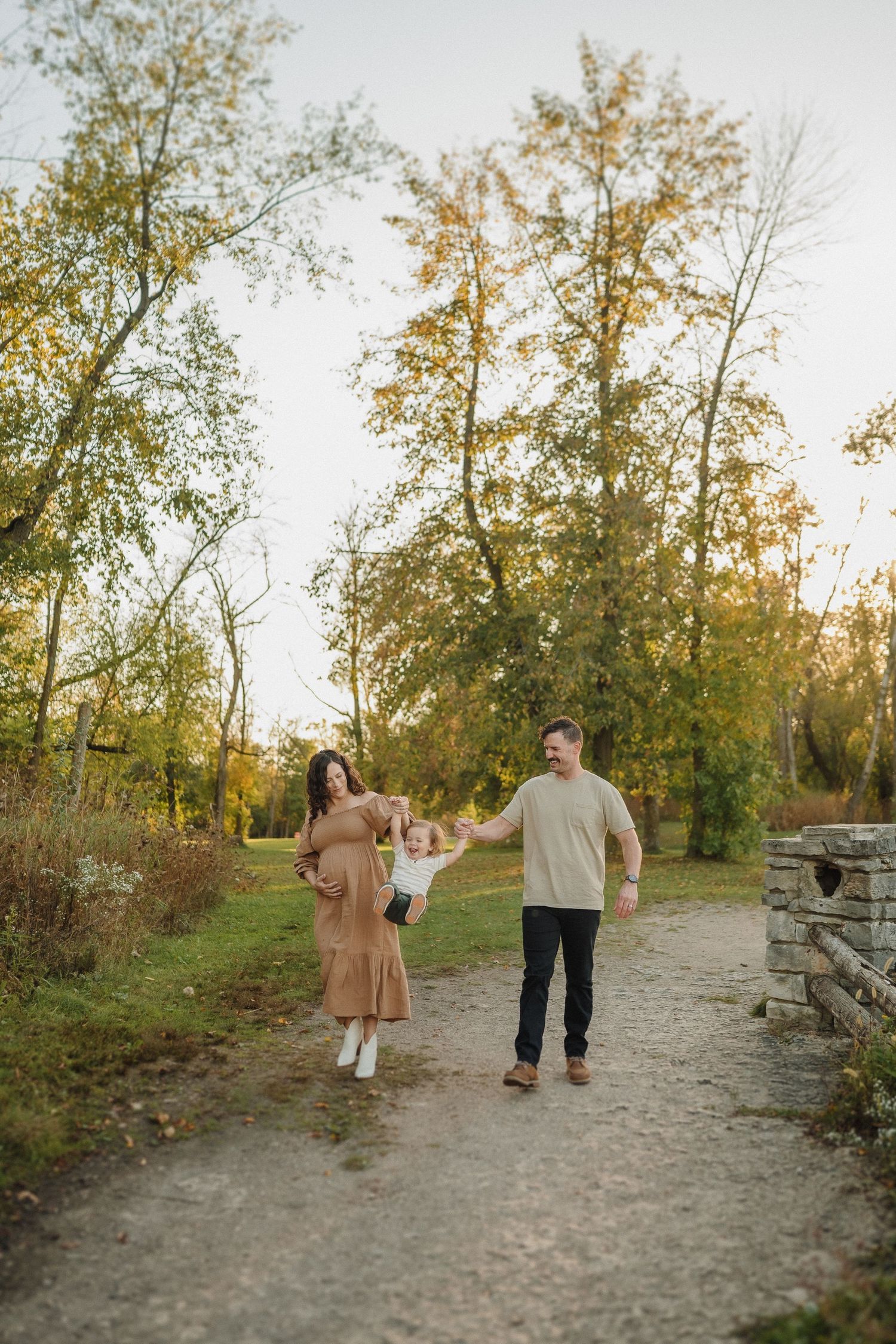 A family walks together on a stone-lined path surrounded by autumn trees at sunset.