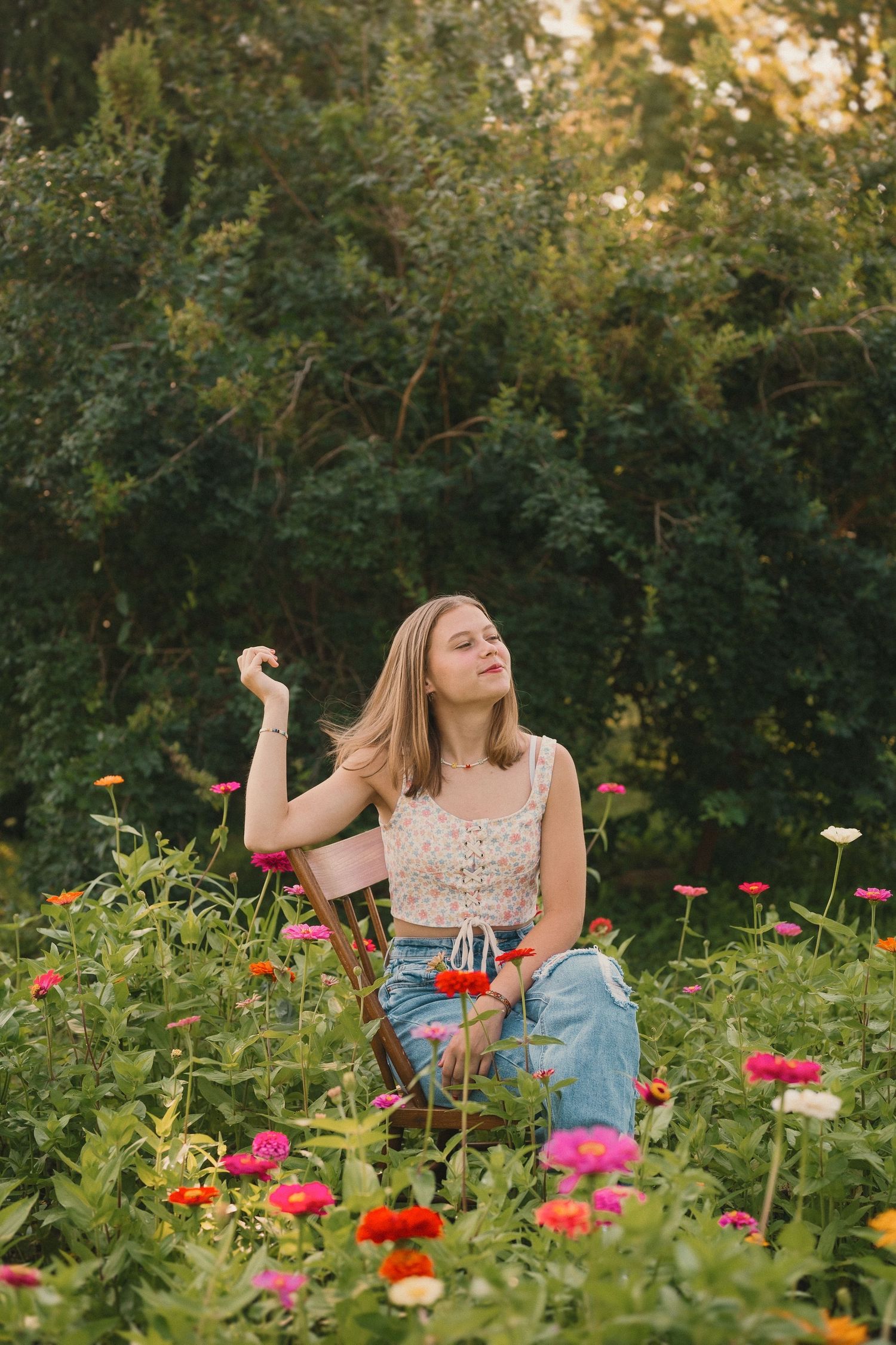 Someone wearing a lace crop top and jeans lounges serenely among vibrant pink and red wildflowers in a garden setting.