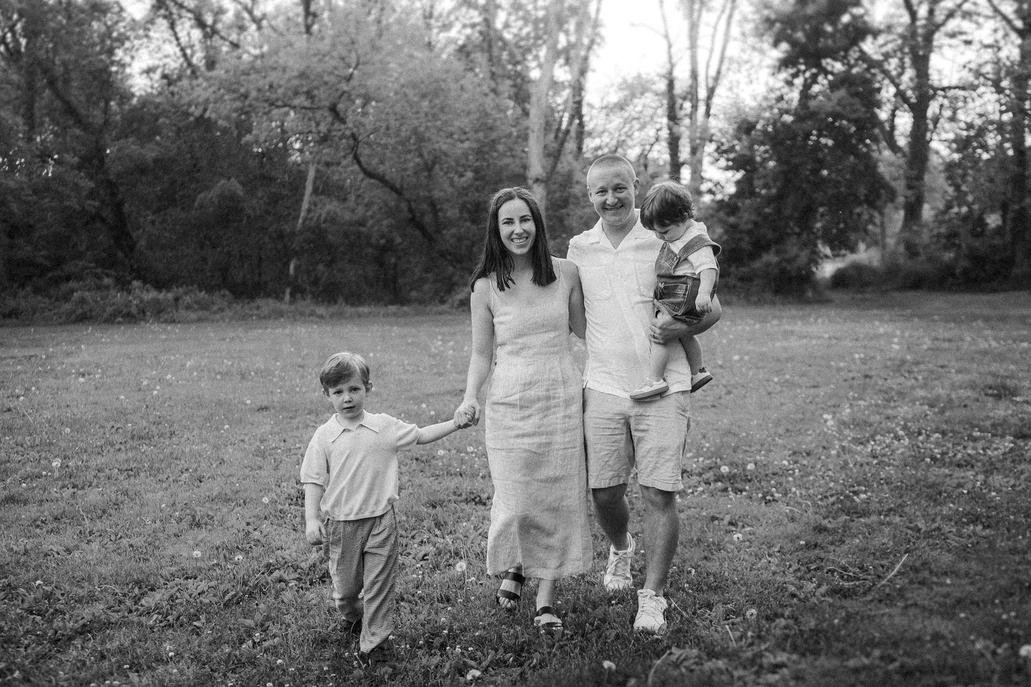 A joyful family in casual clothing walks together through a grassy field on an autumn day.