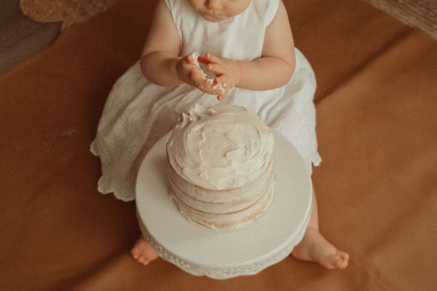 Overhead view of a white tiered cake on a decorative stand during a cake smash session.