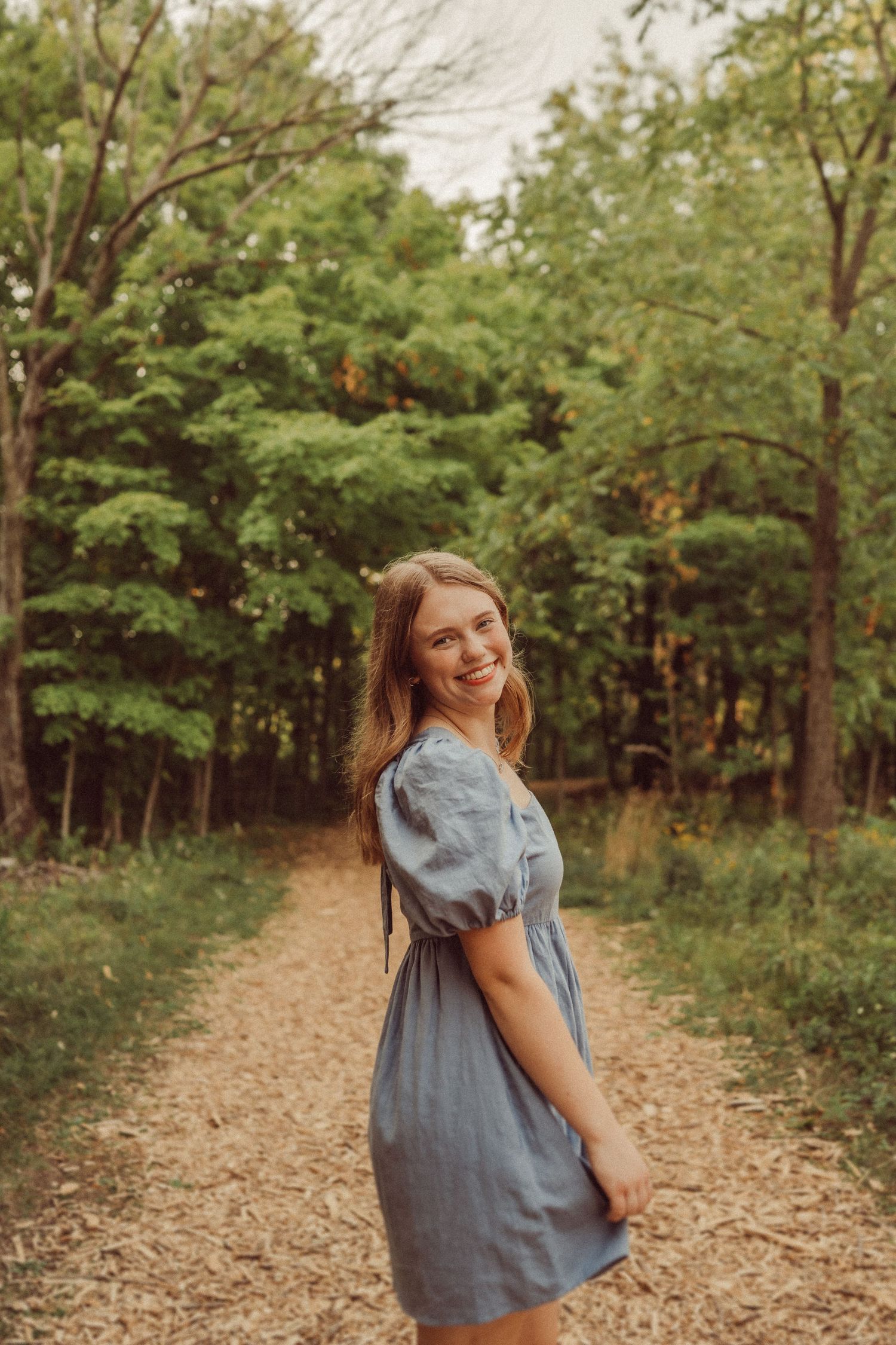 A joyful summer portrait in a blue dress on a sunlit forest path.