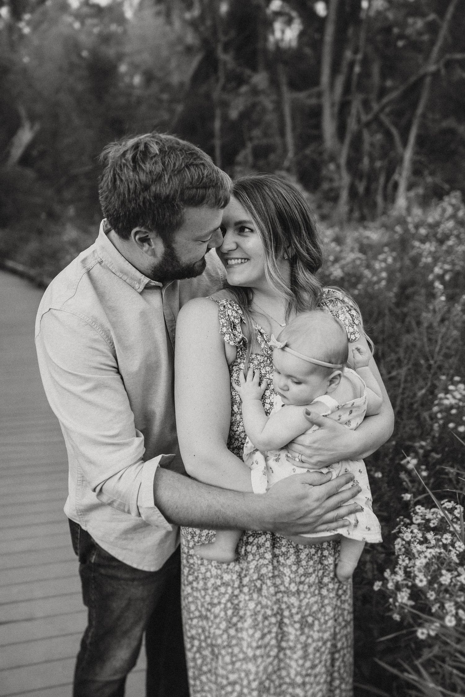 A heartwarming family moment captured in black and white on a wooden walkway surrounded by nature.
