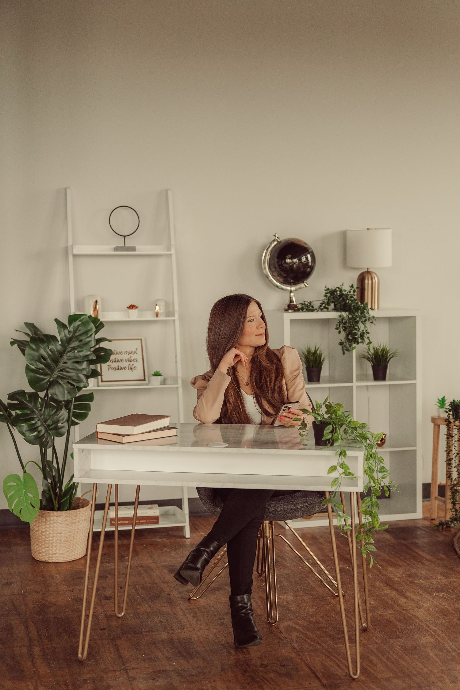 Stylish workspace features desk with hairpin legs, ladder shelf, and potted plants against neutral wall.